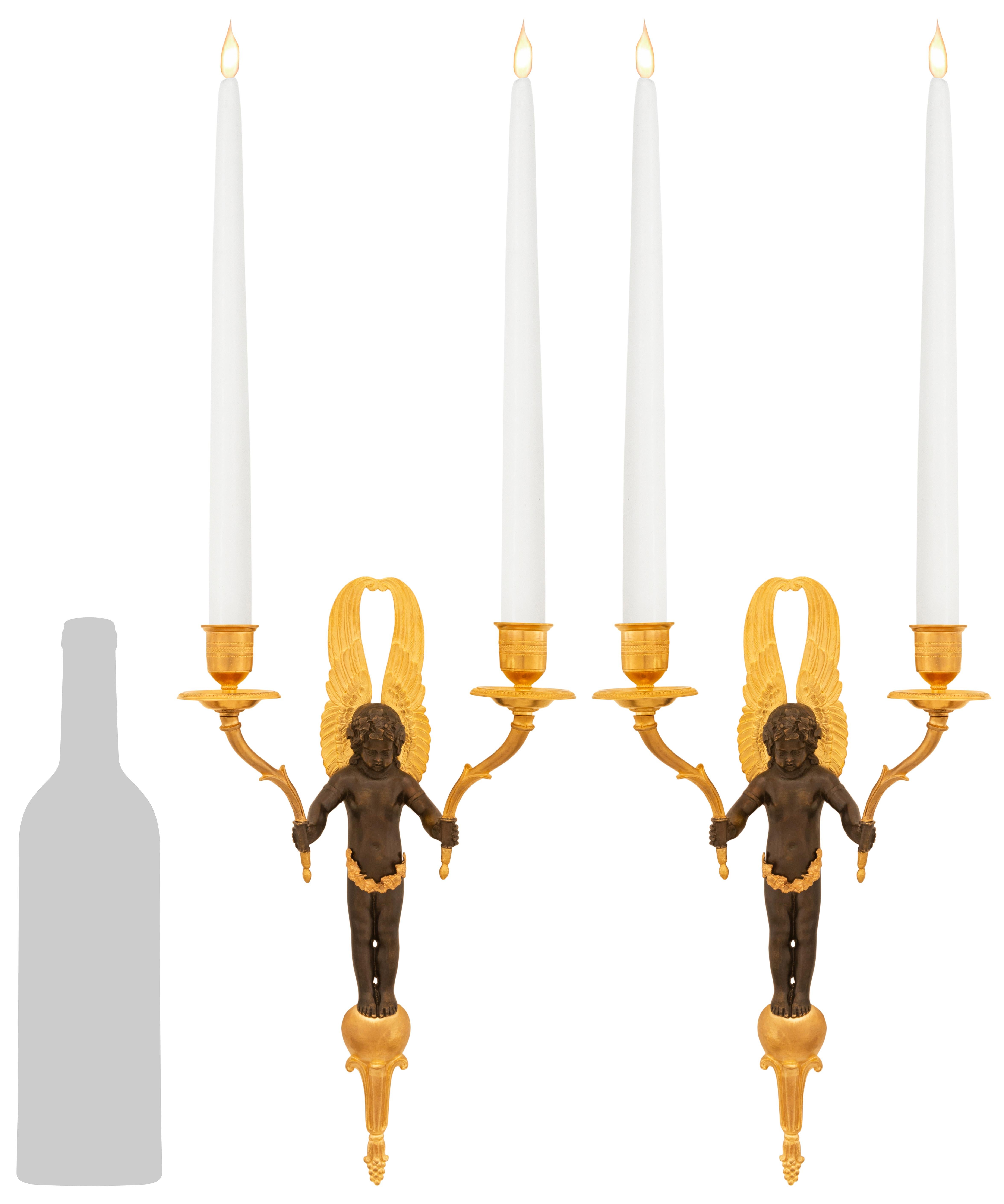 Pareja elegante y de gran calidad de apliques franceses del siglo XIX de Bronce patinado y Ormolu, de estilo Imperio. Cada candelabro de dos brazos está centrado por un bello remate inferior foliado en el que aparecen los encantadores querubines
