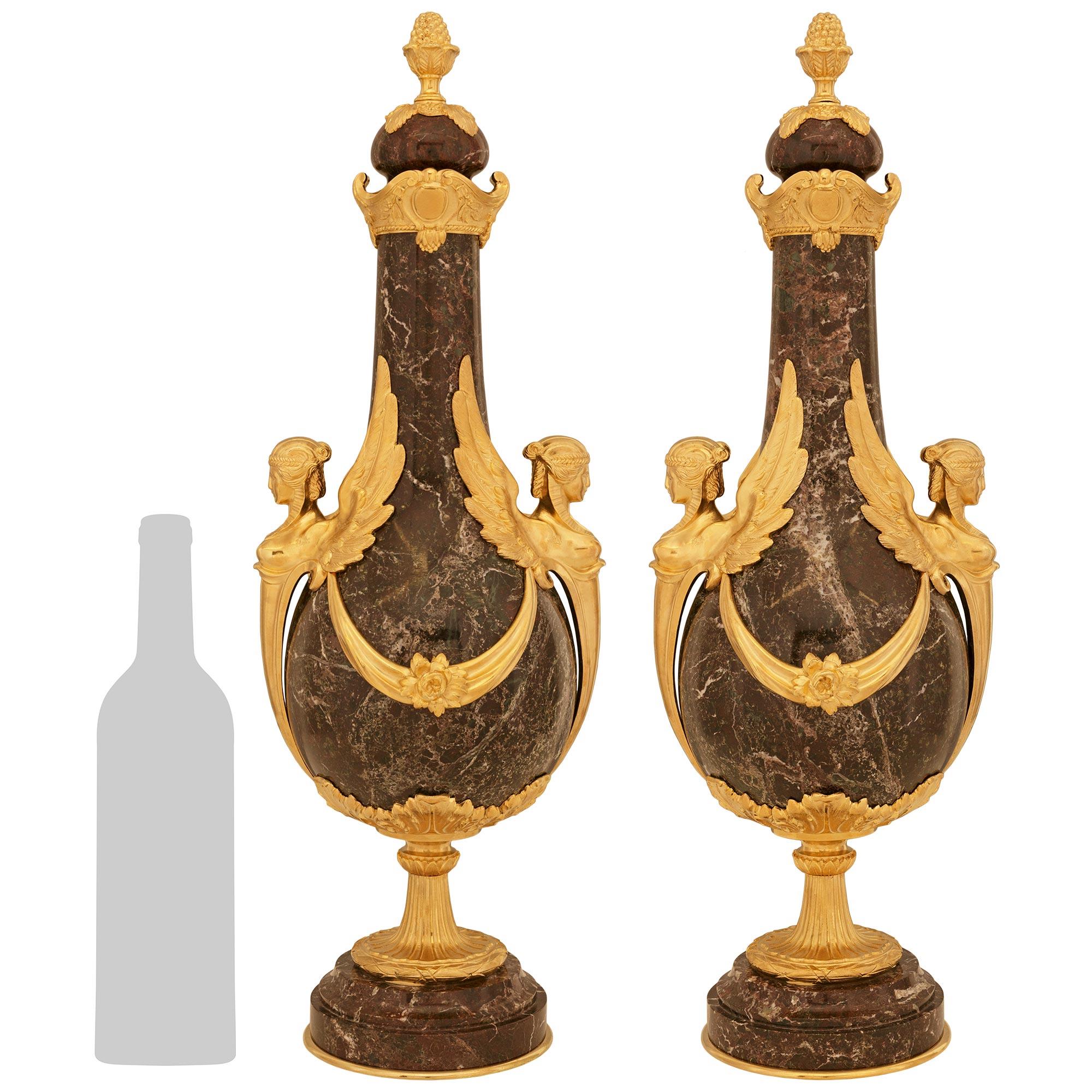 Coppia molto decorativa di urne in marmo Rouge de France e Ormolu in stile Impero del XIX secolo. Ogni meravigliosa urna con coperchio è sollevata da una base circolare in marmo ormolu che sostiene il piedistallo a socle in ormolu con una fascia di