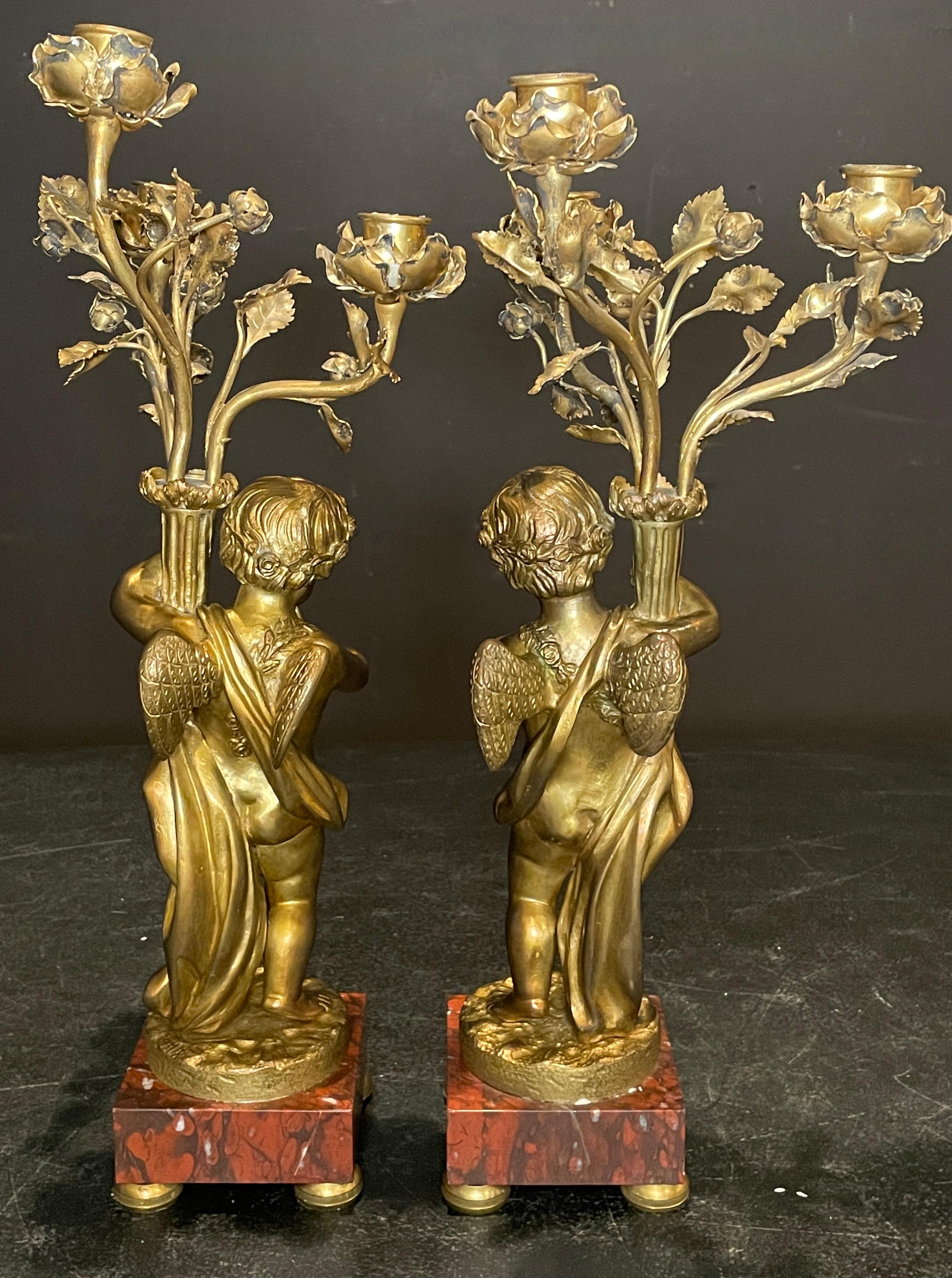 Gilt bronze winged cupid sculpture candelabra mounted on square rouge marble plinths. Louis XVI form with rose pedal candle arms.