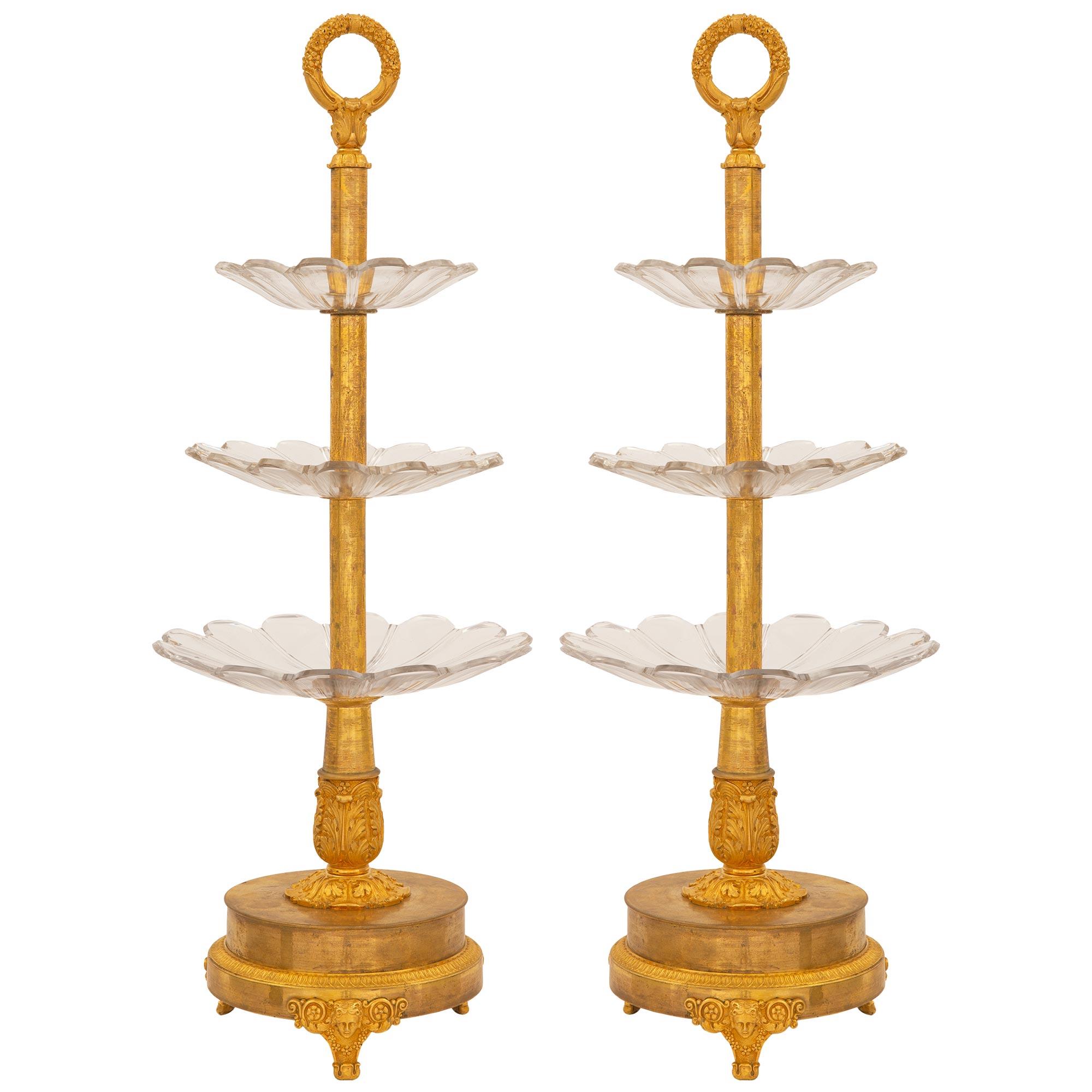 A magnificent pair of French early 19th century First Empire Neo-Classical st. Baccarat and ormolu three level Présentoirs. Each is raised on a circular ormolu base and has finely chased supports with a centered maidens face amidst floral garlands