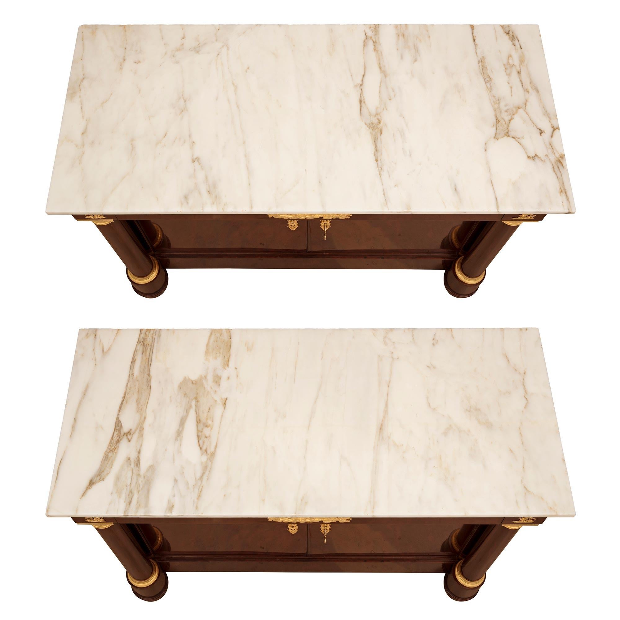 Un'impressionante coppia di buffet francesi del primo Ottocento in mogano fiammato, ormolu e marmo bianco di Carrara. Ogni buffet a due ante e un cassetto è sollevato da piedi elegantemente arrotondati sotto imponenti colonne architettoniche che