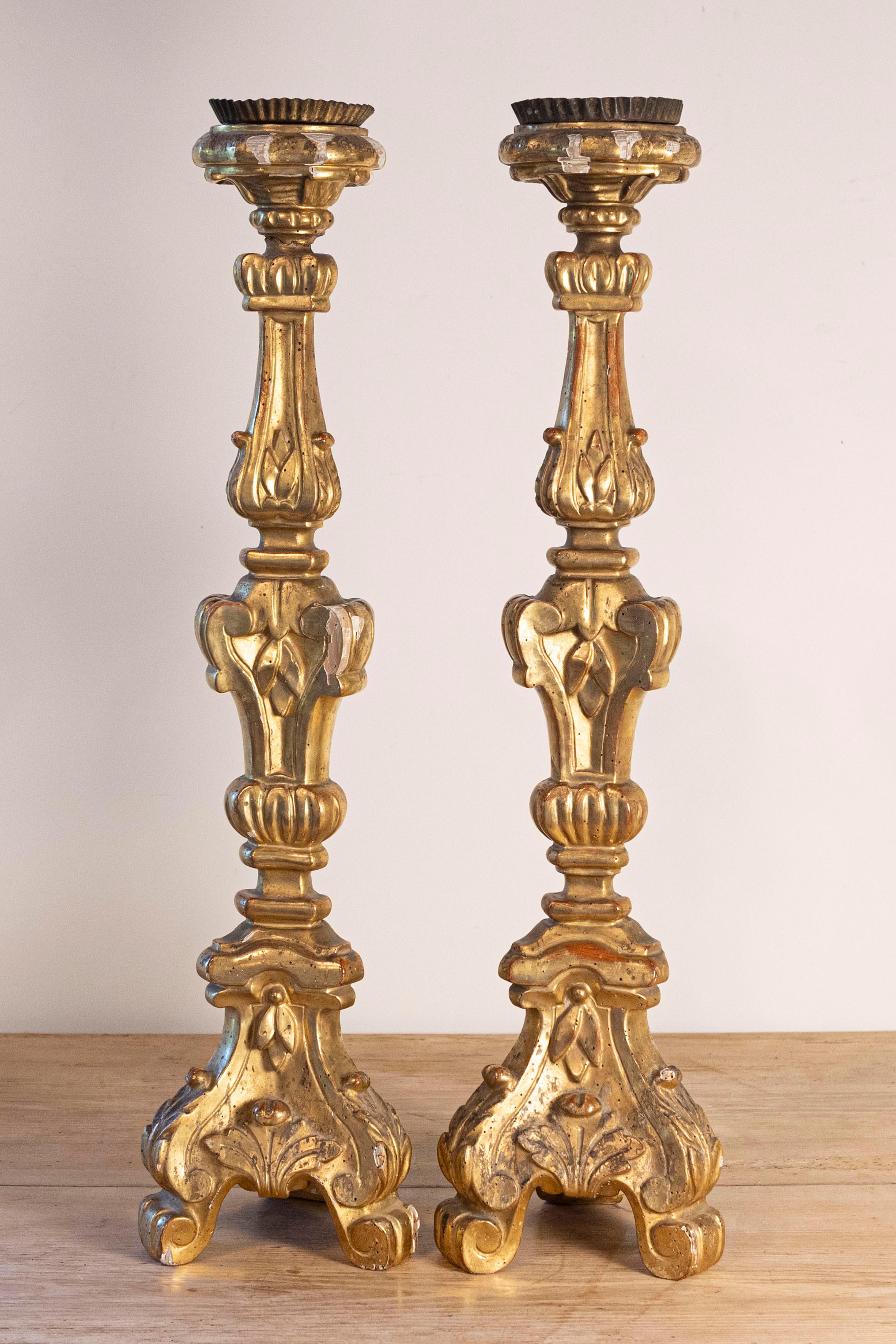 Paire de chandeliers français en bois doré du XIXe siècle, avec volutes et feuillages sculptés. Créée en France au cours du XIXe siècle, cette paire de chandeliers présente un délicat décor de feuillages et de volutes d'un rouge discret. Reposant