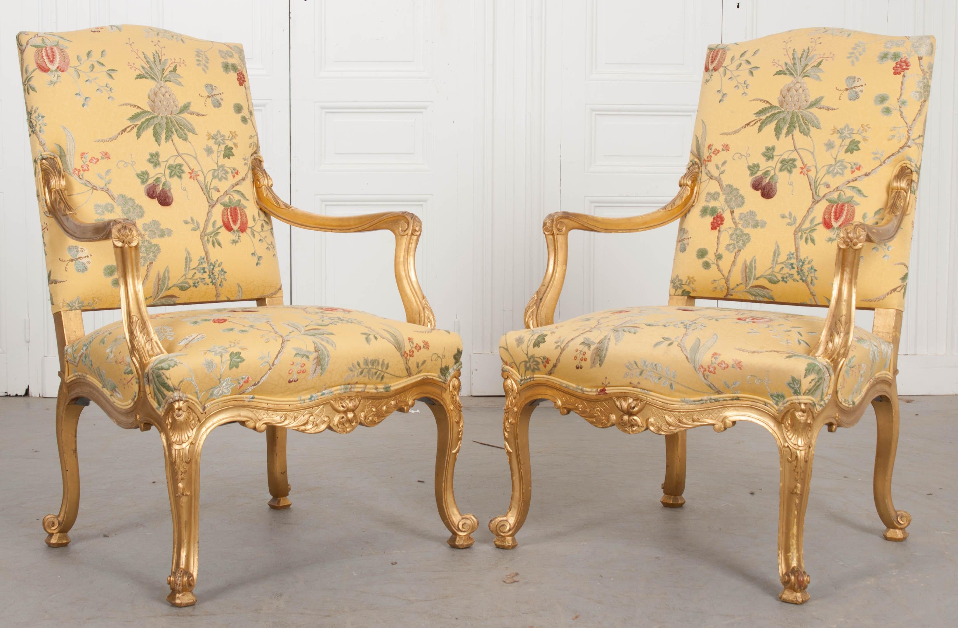 A brilliant pair of gold gilt fauteuils, made in France towards the beginning of the 19th century. The pair have been more recently upholstered in a silk fabric depicting fruiting branches. These Louis XV armchairs have a carved frame that is
