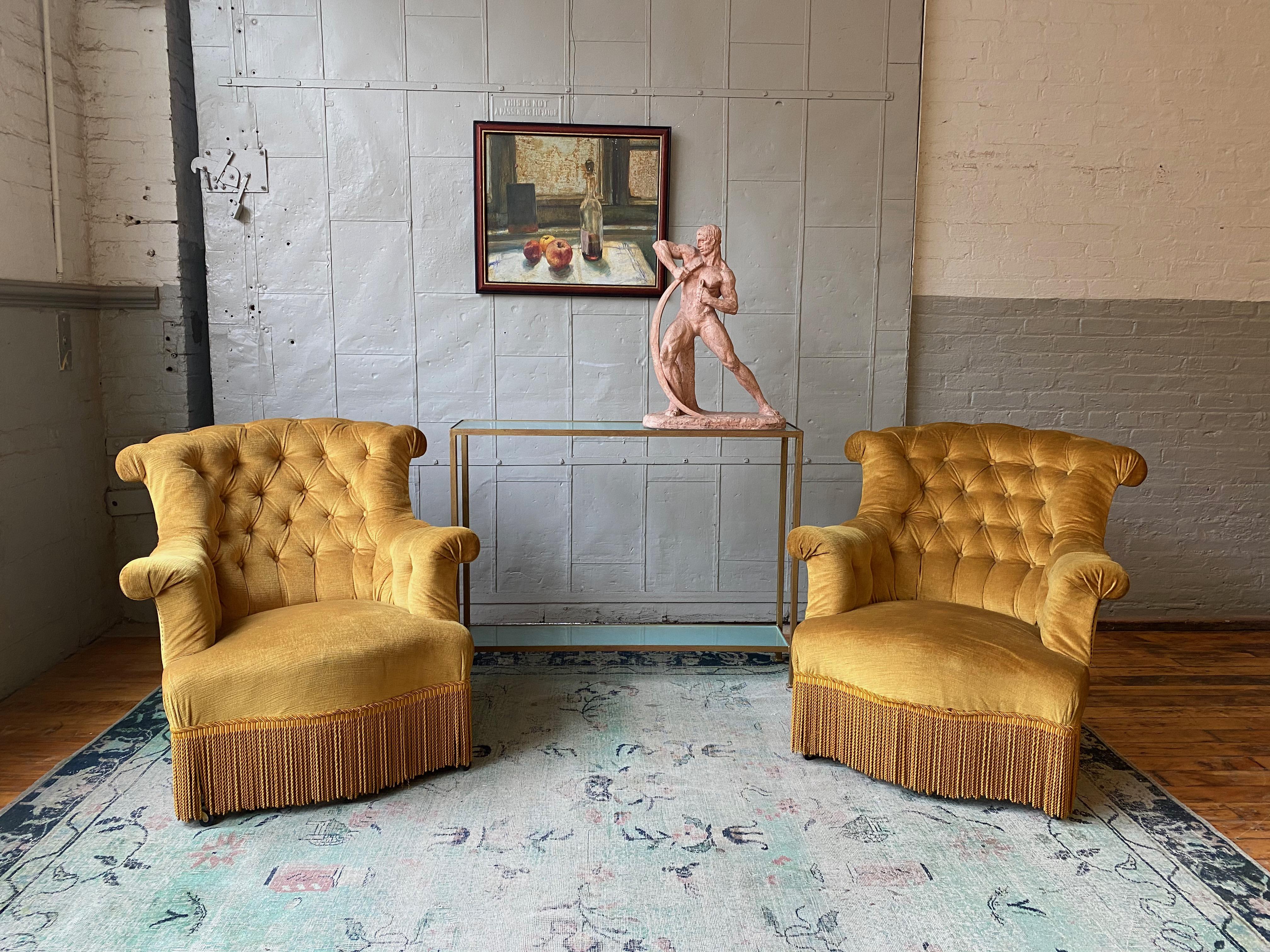 Pair of larger scale French Napoleon III armchairs in gold velvet with bullion fringe. These chairs have unusual rolled 