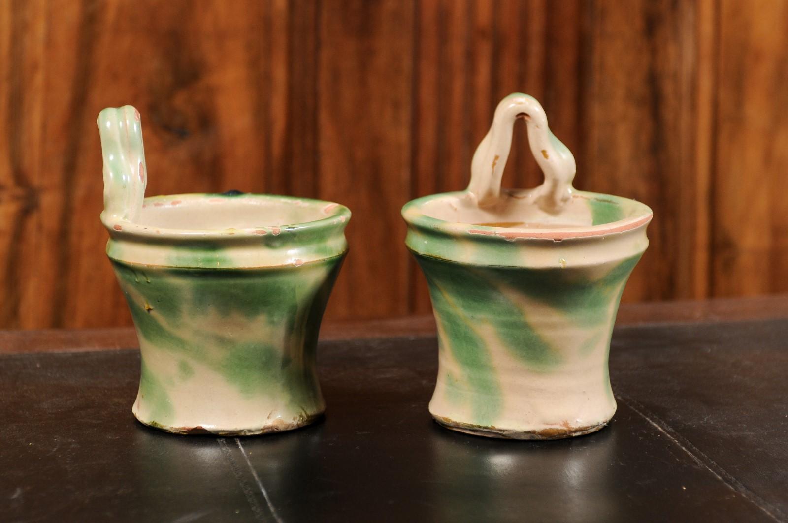 A pair of rustic French pottery hanging planters from the 19th century, with green and yellow glaze. Created in France during the 19th century, each of this pair of hanging planters features a circular curving body adorned with green and yellow