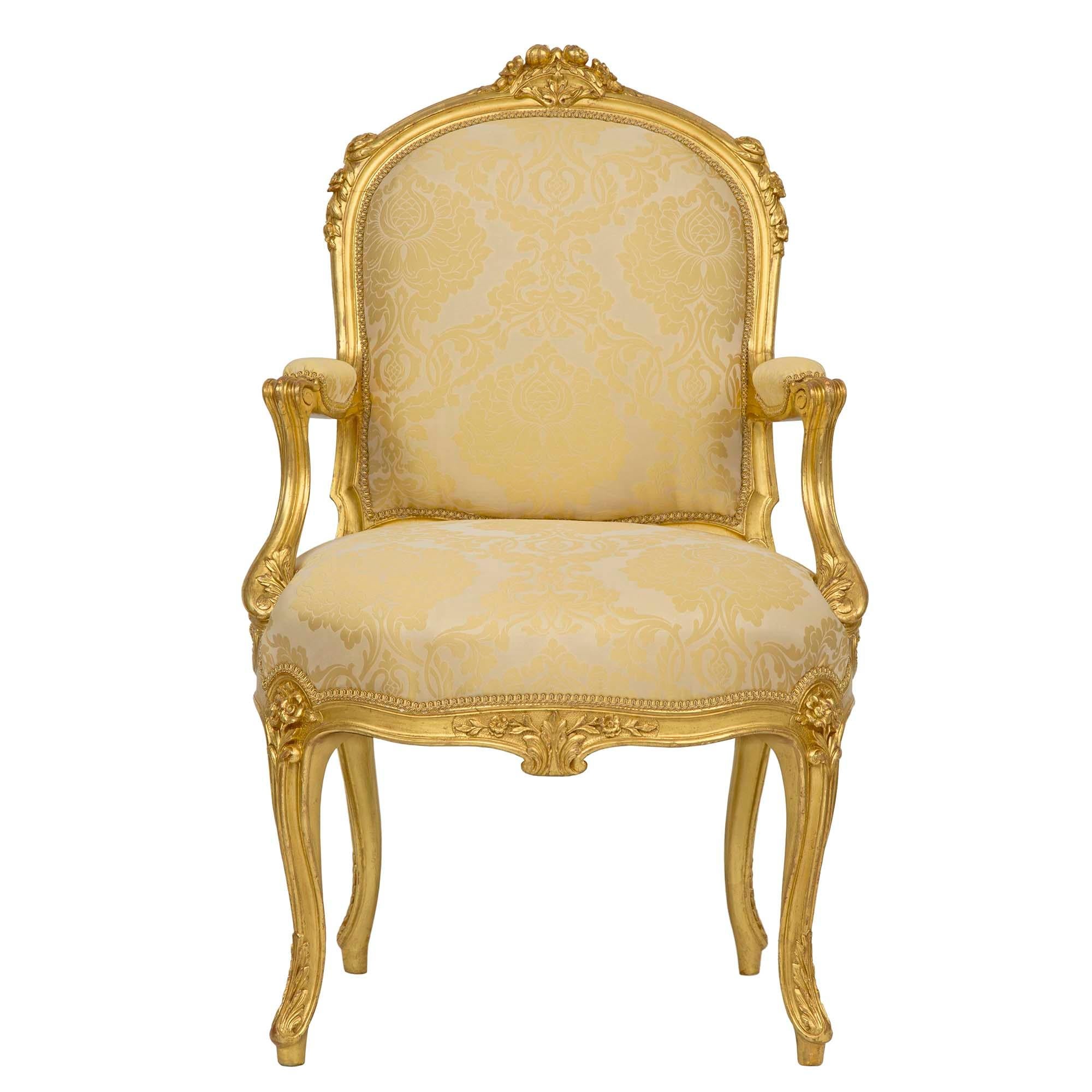 A stunning pair of French 19th century Louis XV st. giltwood armchairs. Each chair is raised on slightly curved legs with acanthus leaf carvings at the base and floral stem at the top. The arbalest frieze is centered with a foliate carved reserve.