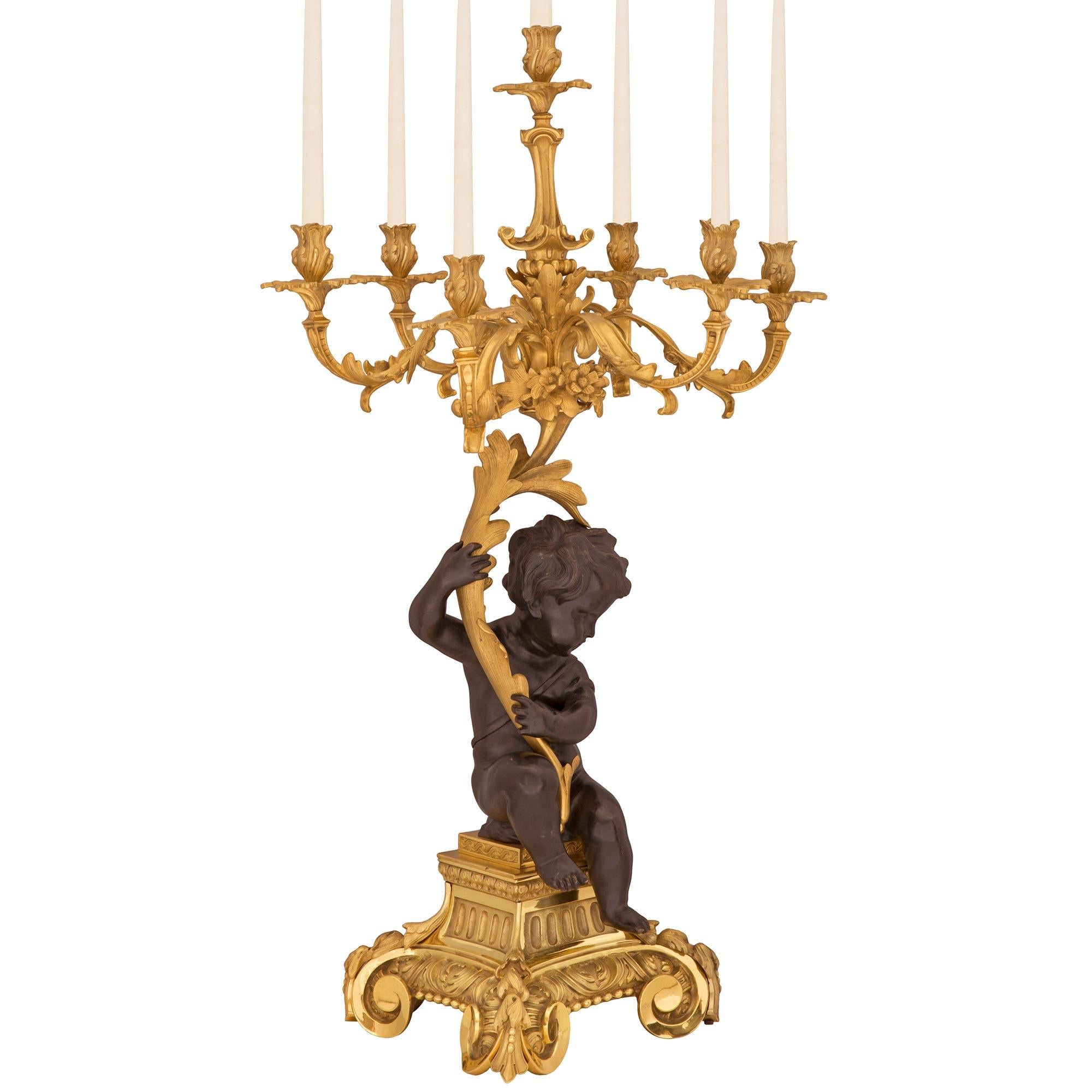 A spectacular and monumentally scaled true pair of French 19th century Louis XV st. ormolu and patinated bronze candelabras. Each seven arm candelabra is raised by a most impressive ormolu square base with stunning scrolled supports in a striking
