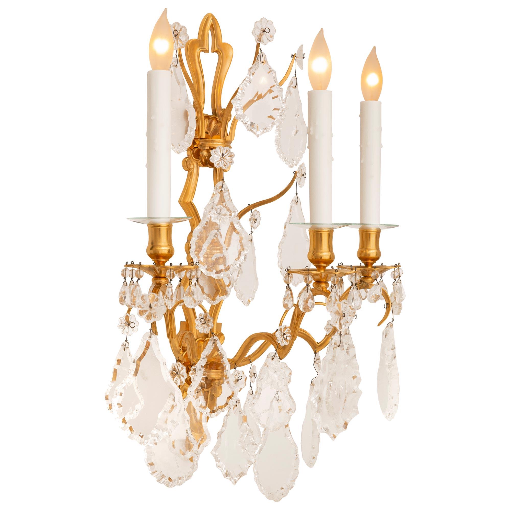 An elegant and finely detailed pair of French 19th century Louis XV st. Ormolu and Rock Crystal sconces. Each scrolling three arm sconce is tastefully decorated with large scaled scalloped Rock Crystals with smaller scale scalloped Rock Crystals