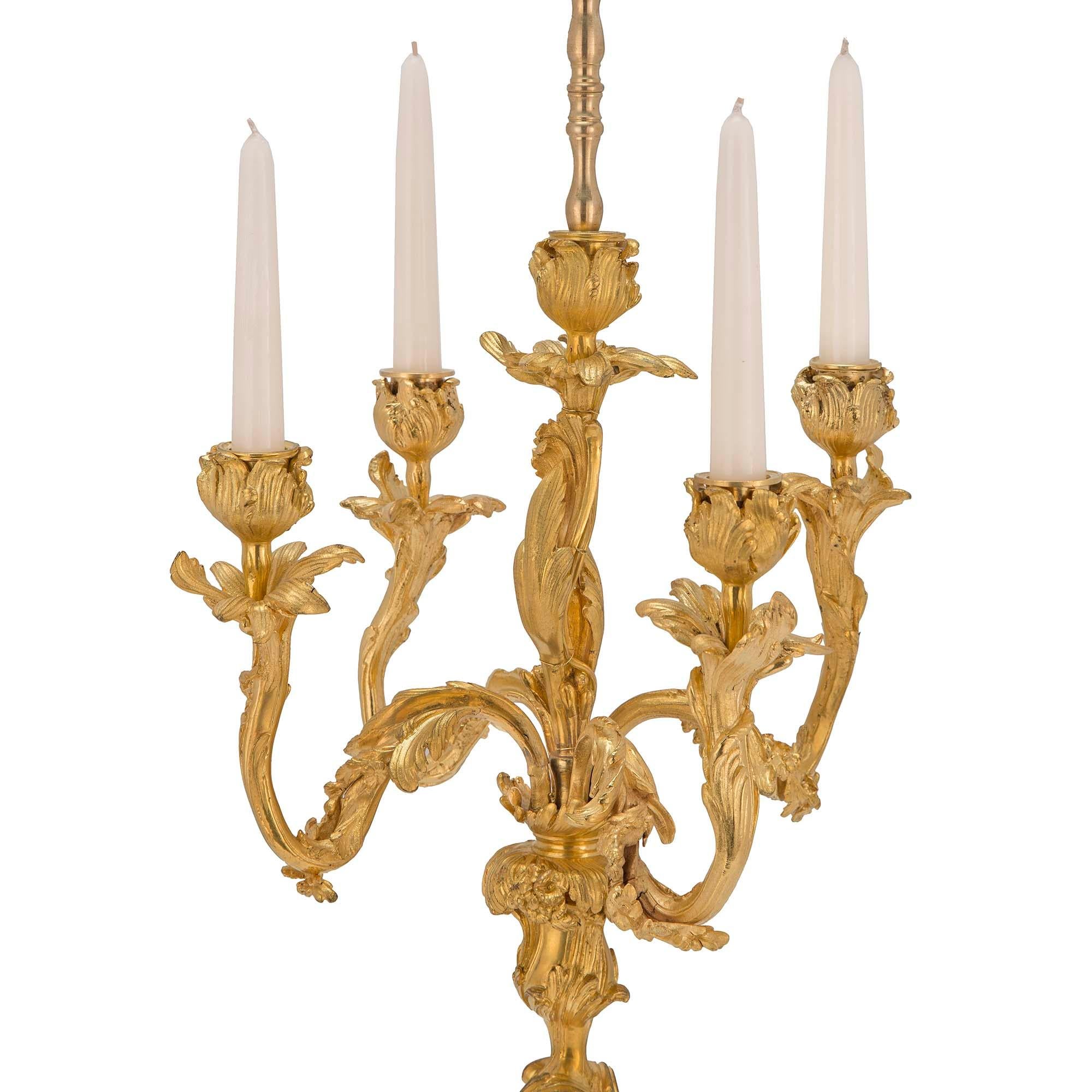 Une belle paire de lampes candélabres françaises du 19ème siècle en st. Louis XV et bronze doré. Chaque lampe repose sur des pieds latéraux rectangulaires concaves, sous la base circulaire. La base est accentuée par des feuilles d'acanthe en volutes
