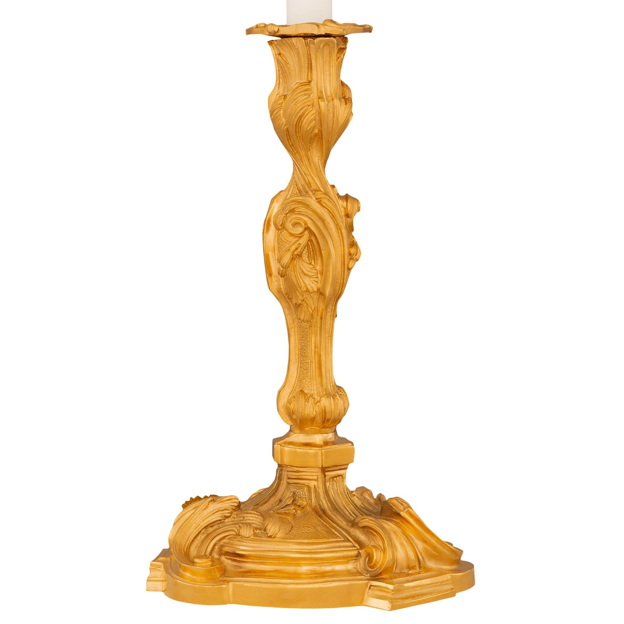 Une élégante paire de lampes-bougies en bronze doré de style Louis XV du XIXe siècle. Chaque bougeoir monté en lampe est surélevé par une base circulaire avec trois fins éléments en saillie sous de jolis motifs feuillagés en volutes dans une riche