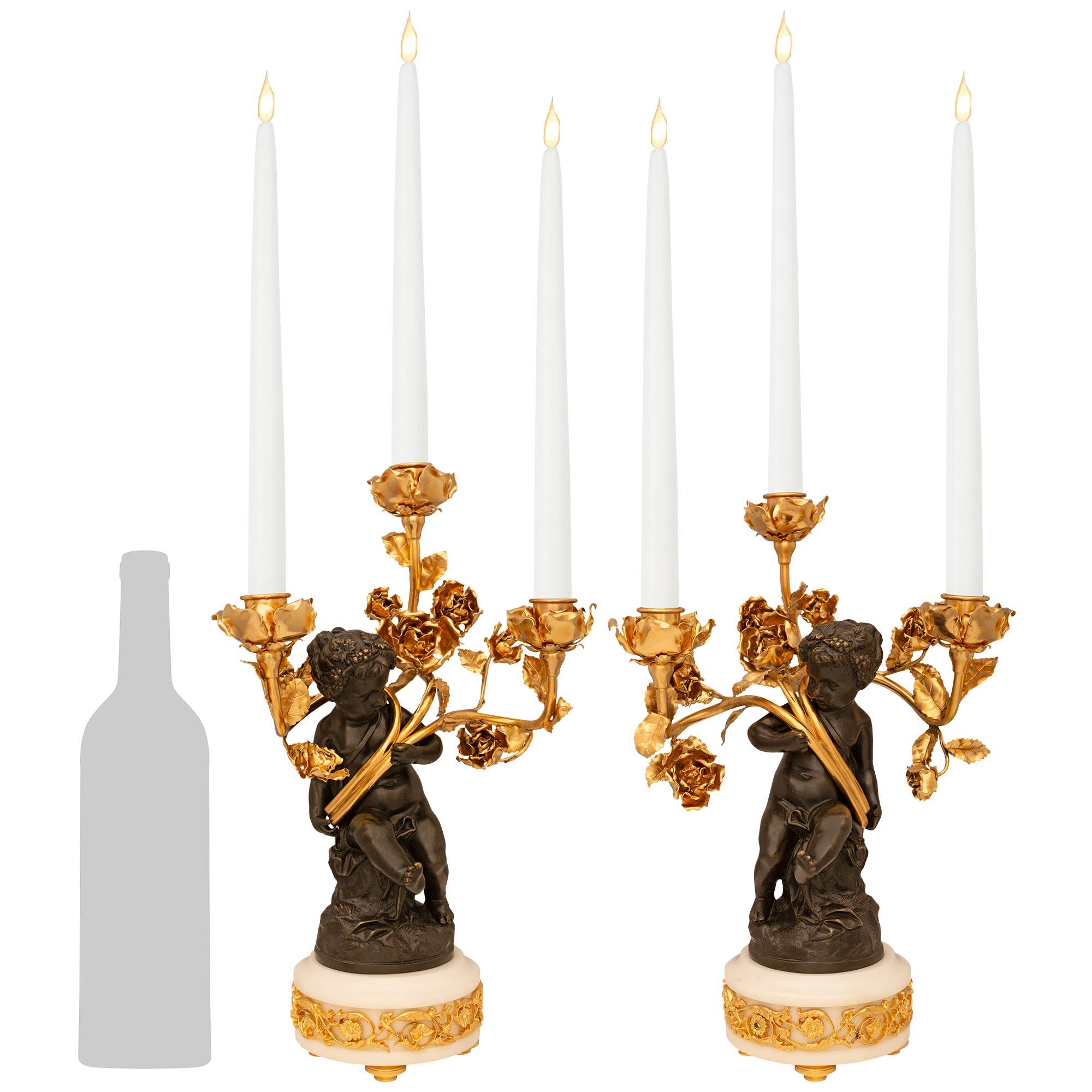 Una splendida e decoratissima coppia di candelabri francesi del XIX secolo in bronzo patinato, marmo bianco di Carrara e Ormolu. Ogni candelabro a tre bracci è sollevato da una base circolare in marmo bianco di Carrara con una fascia concava di