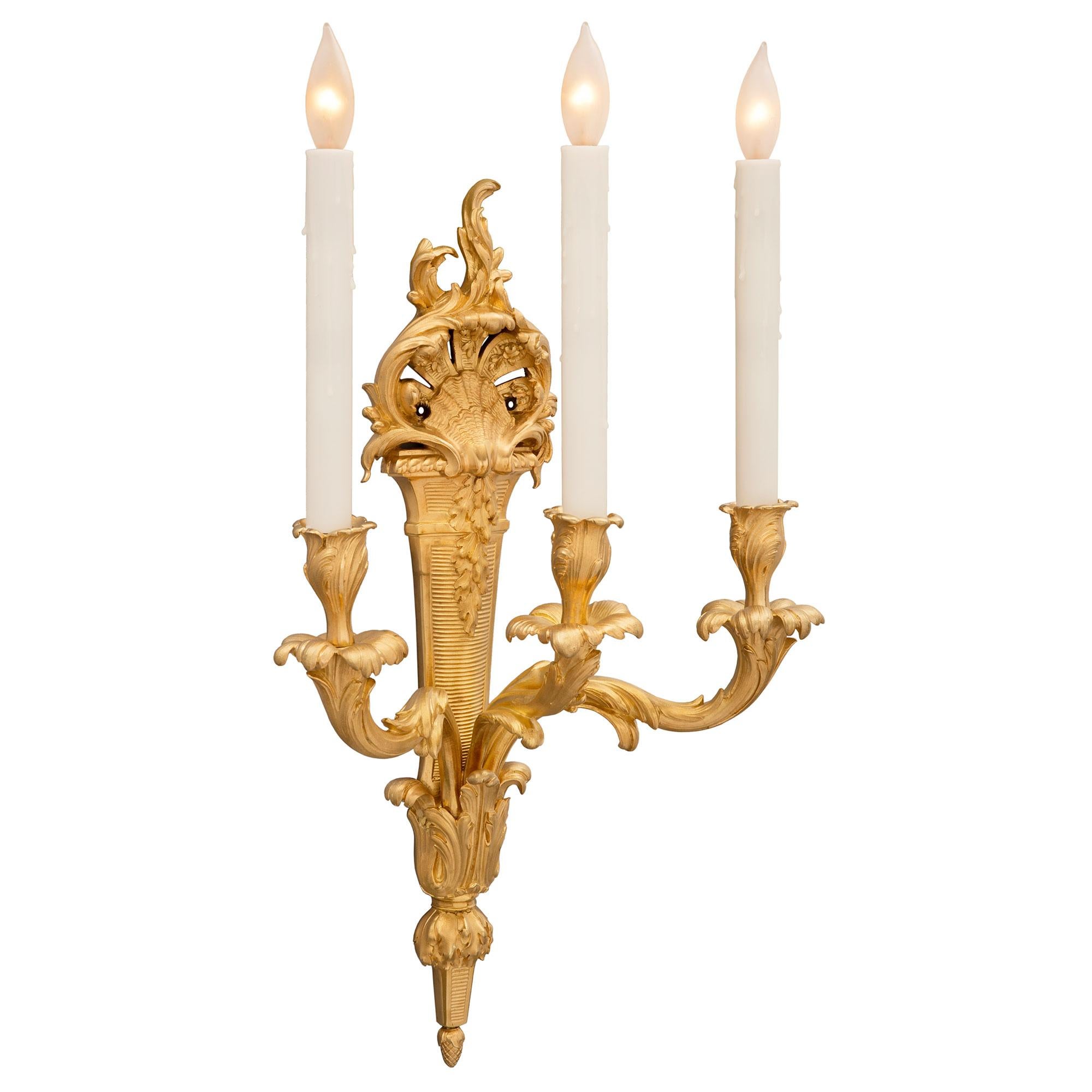 An elegant and most decorative pair of French 19th century Louis XV st. ormolu sconces. Each three-arm sconce is centered by a fine bottom acorn-shaped finial below striking richly chased large acanthus leaves. Each of the beautifully scrolled arms