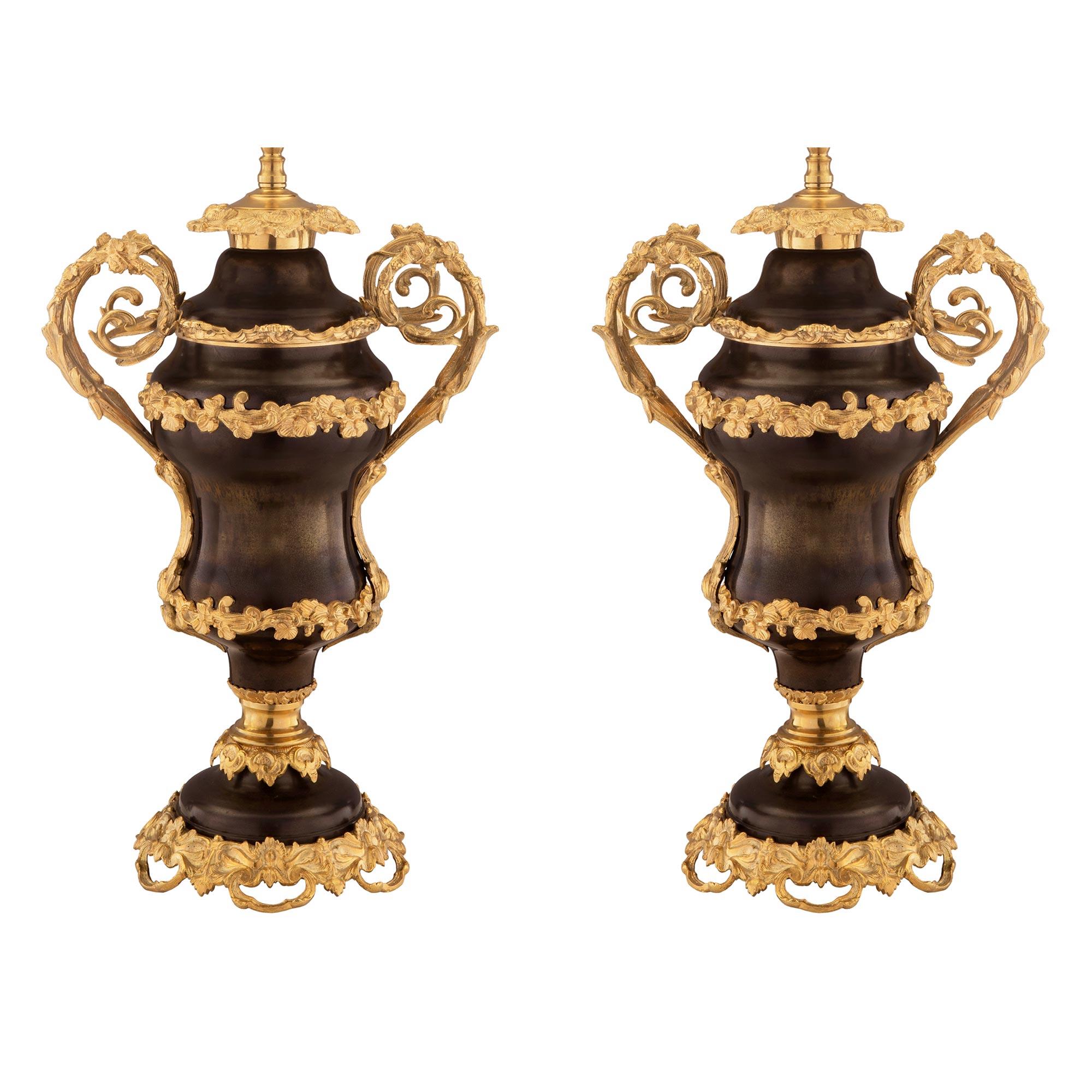 A beautiful and large scale pair of French 19th century Louis XV style patinated bronze and ormolu lamps. Each lamp is raised by lovely ormolu pieced foliated and floral movements below patinated bronze socle pedestals. The elegantly shaped bodies