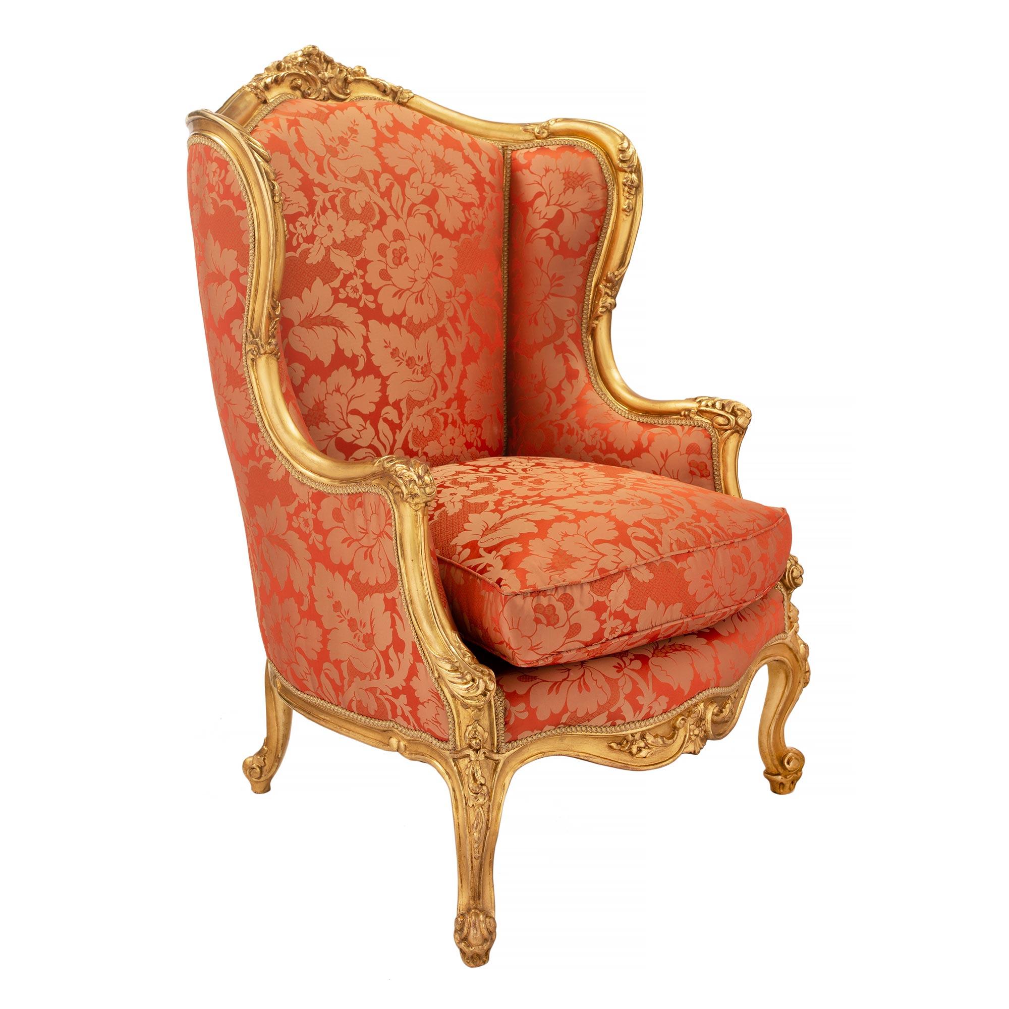 A fine and most elegant pair of French 19th century Louis XV style giltwood Bergères à Oreilles. Each armchair is raised by lovely cabriole legs with scrolled feet and finely detailed floral carvings. The arbalest shaped frieze is centered by
