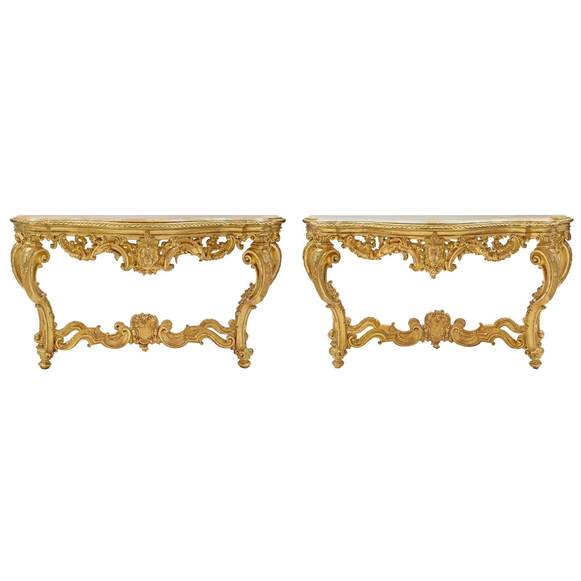 A spectacular and monumental French early 19th century Louis XV st. giltwood and marble consoles with their original palatial companion mirrors. Each console is raised by topie feet and elegant and richly carved scrolled legs, joined by an X
