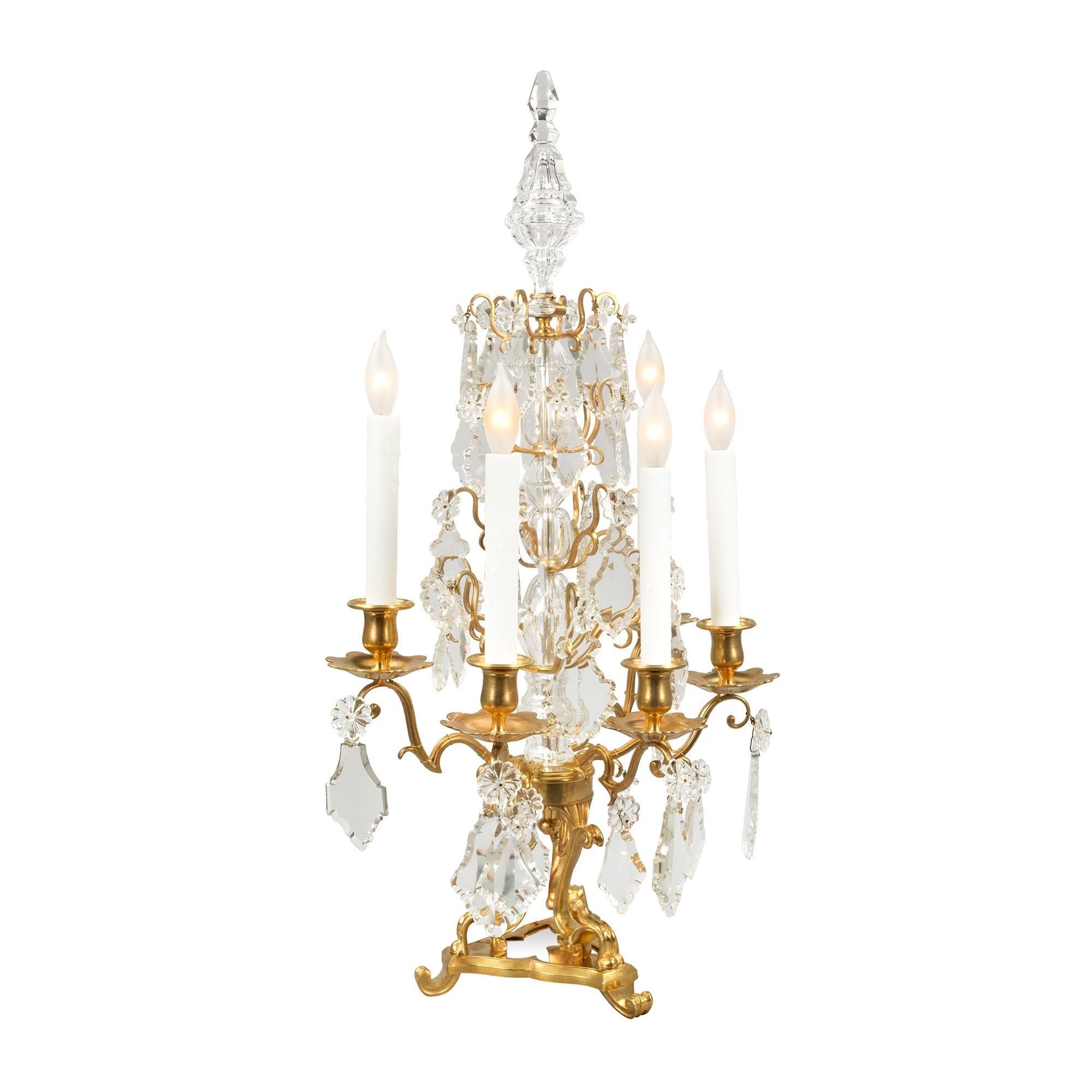 An elegant pair of French 19th century Louis XV st. ormolu and Baccarat Girandoles. Each lamp is raised by a fine triangular ormolu base with most decorative scrolled feet and scrolled supports, centering a silvered bronze base. Each arm displays