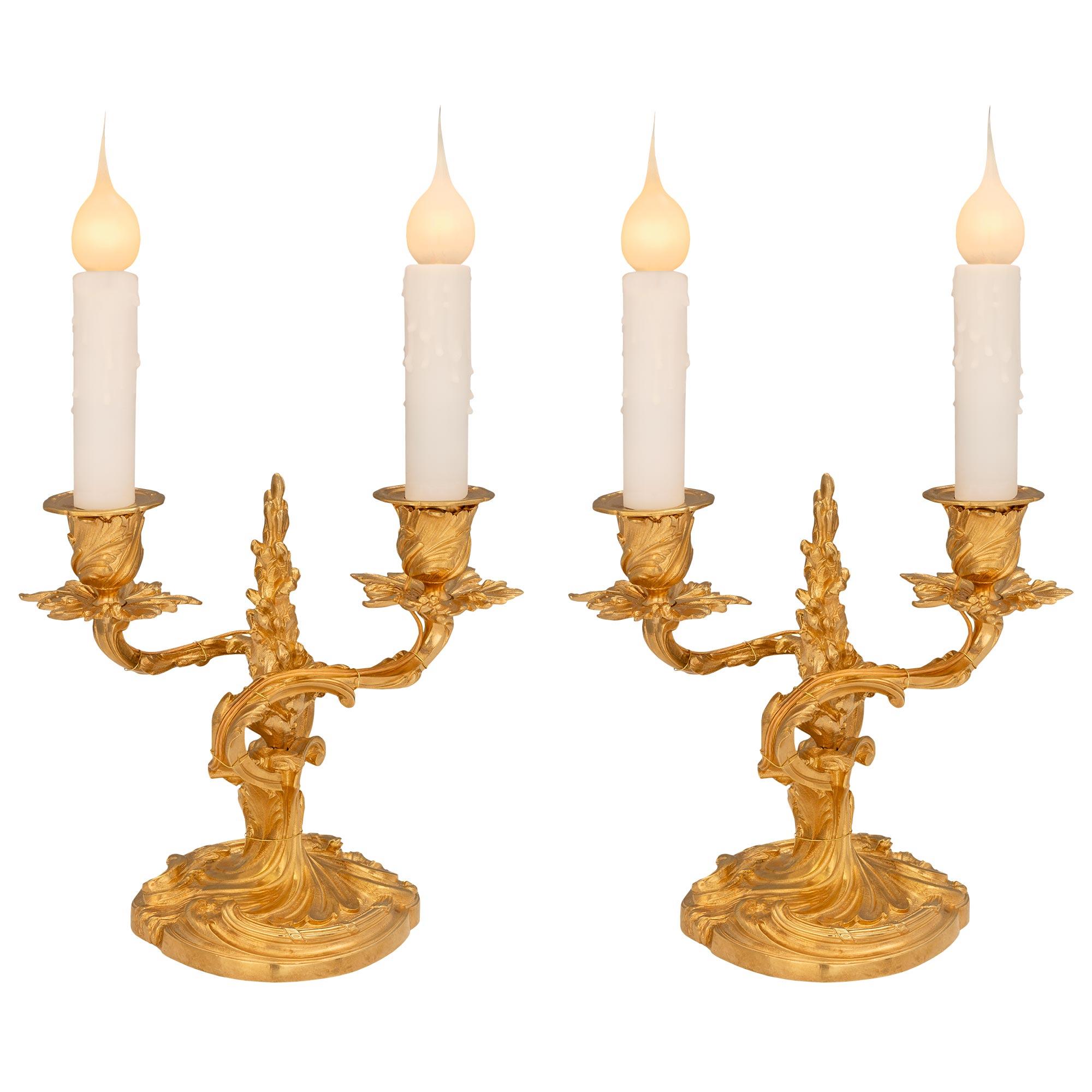 A charming and most elegant pair of French 19th century Louis XV st. ormolu candelabra lamps. Each lamp is raised by a circular foliate base with a beautiful central fut in a striking satin and burnished finish. The two elegantly scrolled arms are