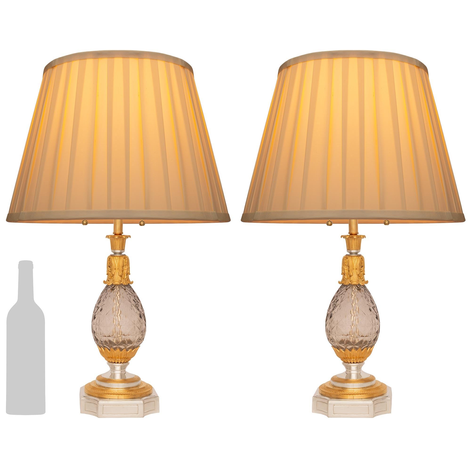 An elegant pair of French 19th century Louis XVI st. Baccarat crystal, Silvered Bronze and Ormolu lamps. Each lamp is raised by a Silvered Bronze base with a recessed pattern and concave corners. Leading up are richly chased Ormolu and Silvered