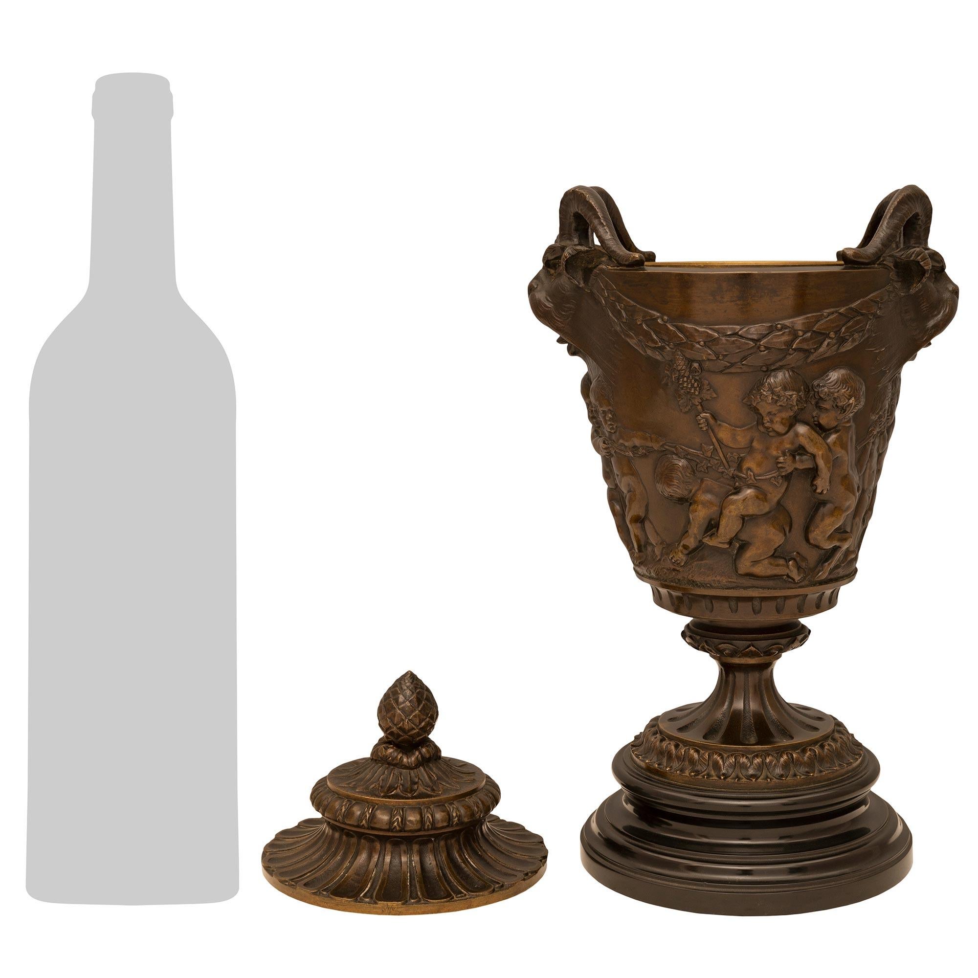Charmante paire d'urnes en bronze patiné et marbre noir belge de style Louis XVI du XIXe siècle, signées Clodion et attribuées à Barbedienne. Chaque urne est surmontée d'une belle base circulaire en marbre noir tacheté de Belgique, sous l'élégant