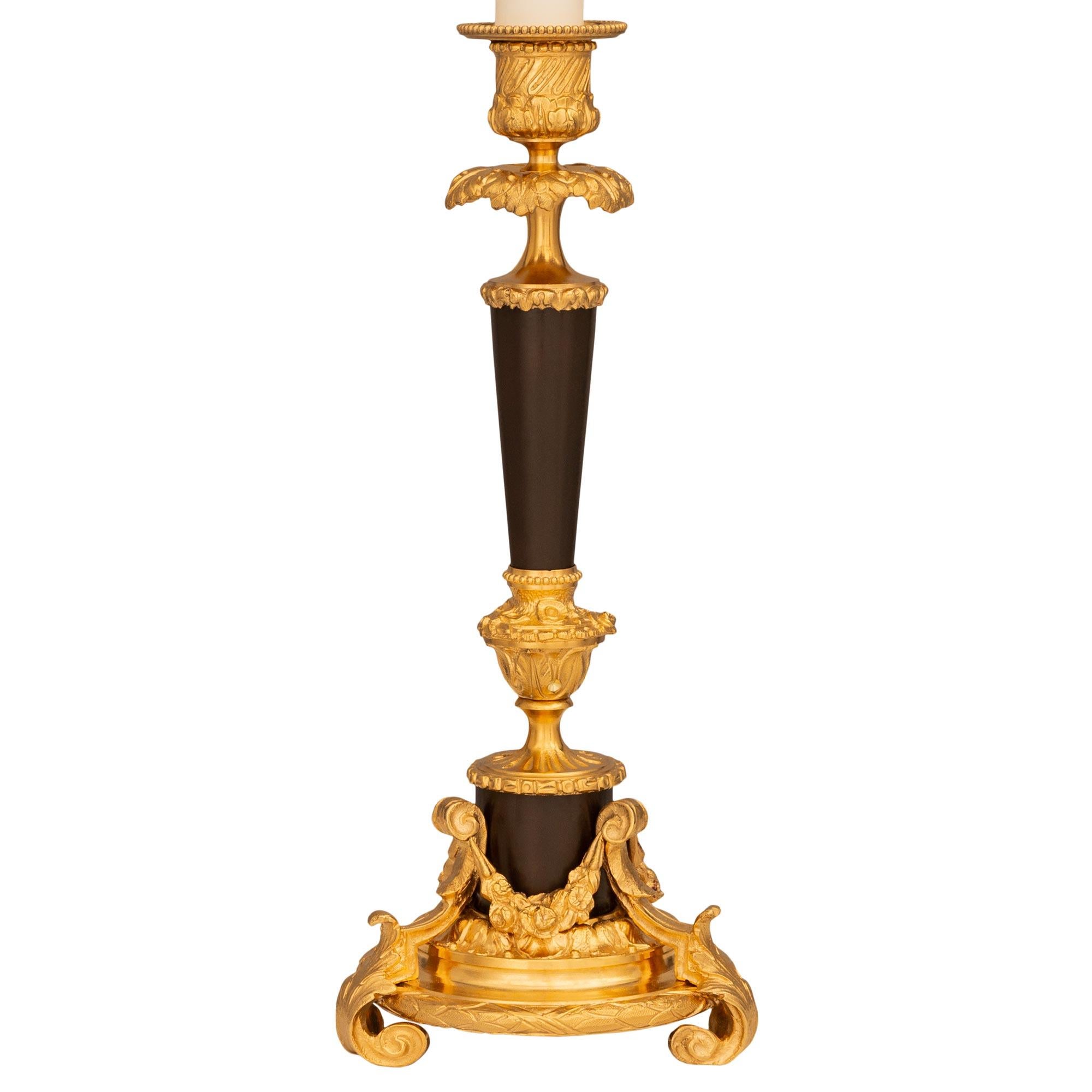 A striking and most elegant pair of French 19th century Louis XVI st. Ormolu and patinated Bronze candlestick lamps. Each lamp is raised on a remarkable circular Ormolu base with three scrolled acanthus leaf feet connected by a laurel band at the