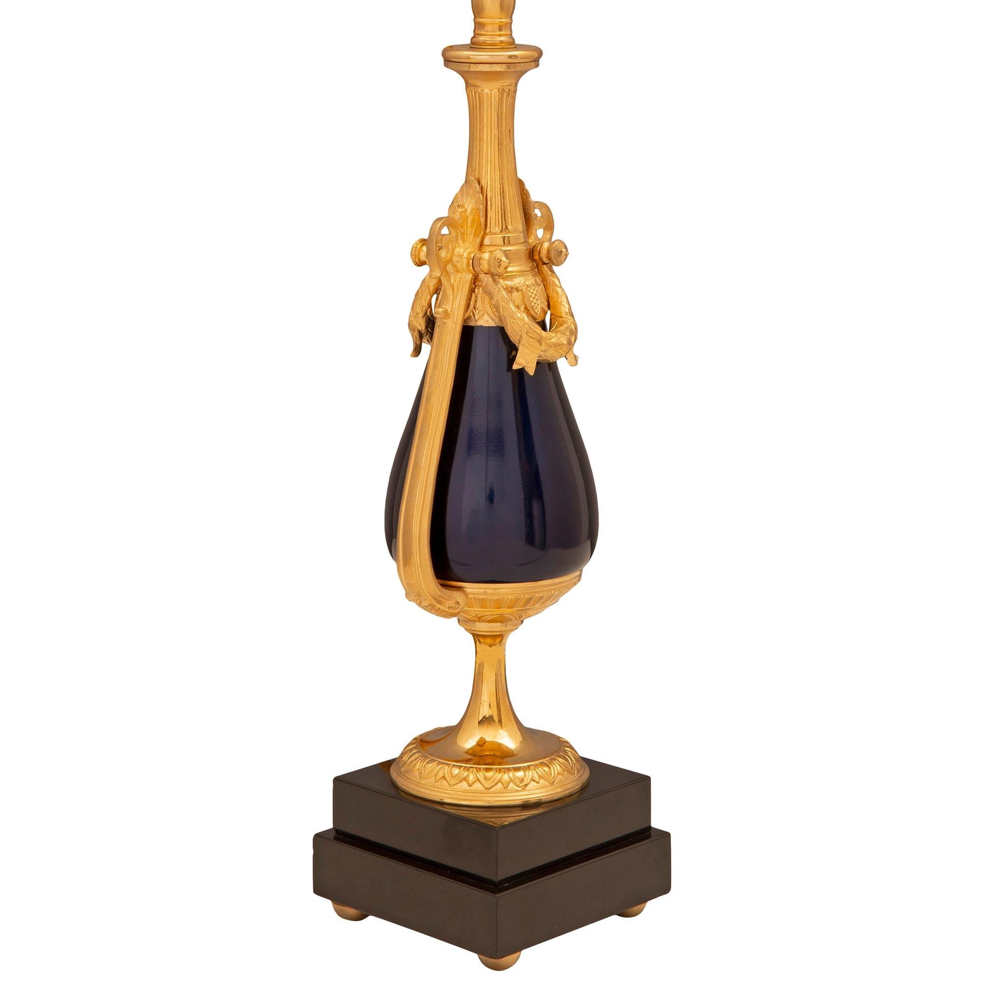 A striking pair of French 19th century Louis XVI st. cobalt blue enameled bronze, ormolu, and black Belgian marble lamps. Each lamp is raised by a square stepped black Belgian marble base with fine ormolu ball feet. The socle shaped pedestal