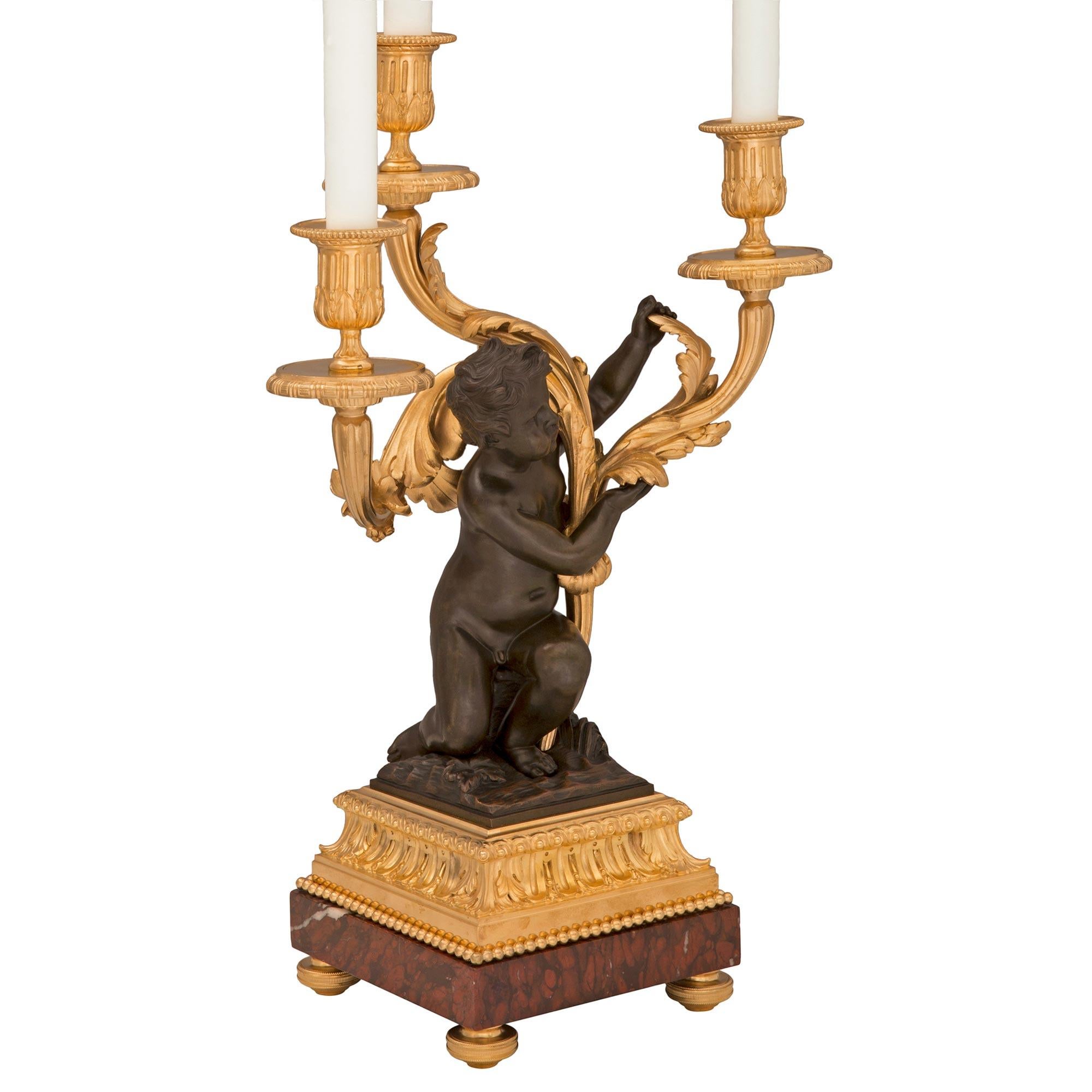 An exquisite true pair of French 19th century Louis XVI st. Belle Époque period patinated bronze, ormolu and Rouge Griotte marble candelabra lamps. Each three arm lamp is raised by elegant topie shaped feet below the Rouge Griotte marble with a fine