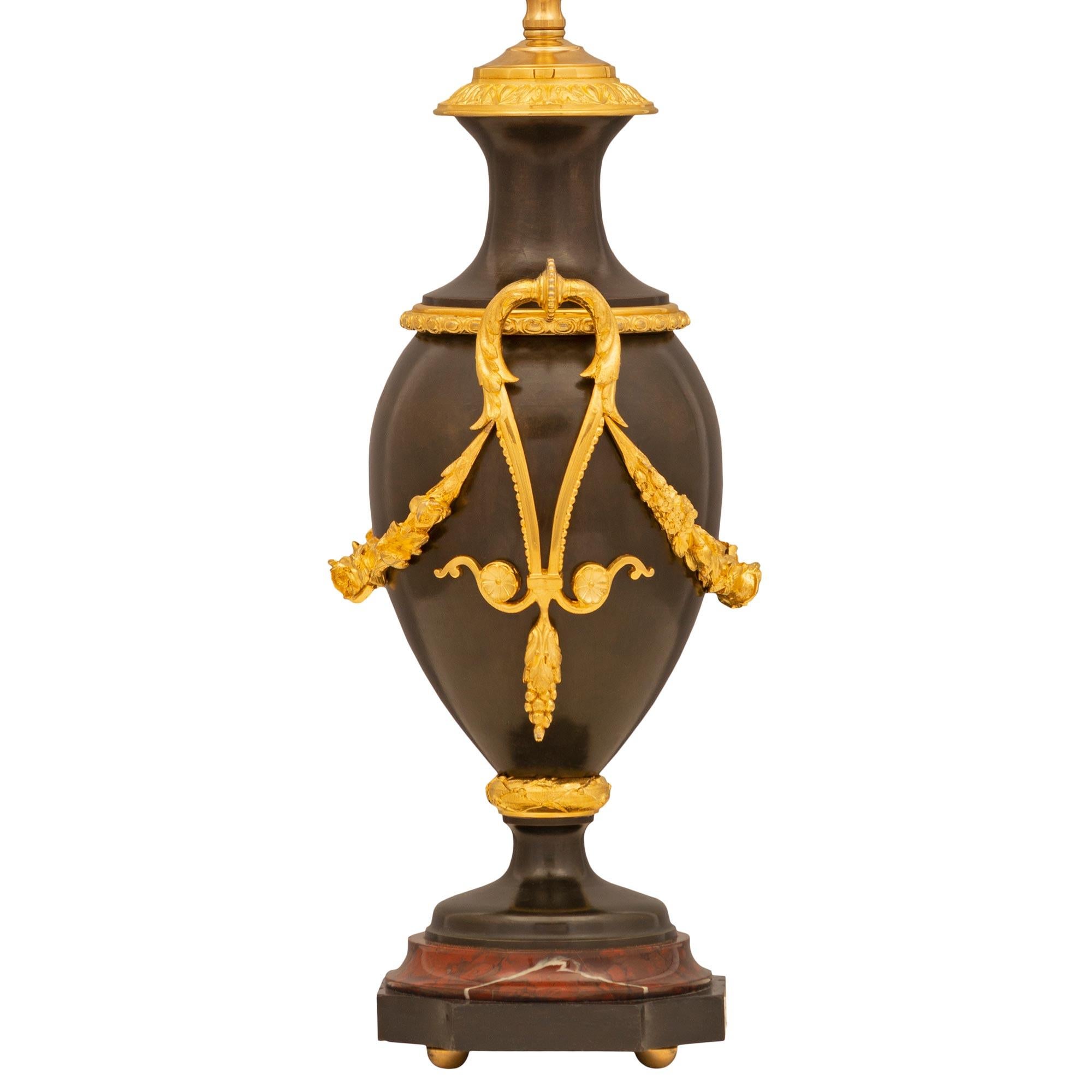 A remarkable pair of French 19th century Louis XVI st. patinated bronze, ormolu, and Rouge Griotte marble lamps. Each lamp is raised by elegant ormolu ball feet below the square patinated bronze base with concave corners and a most decorative