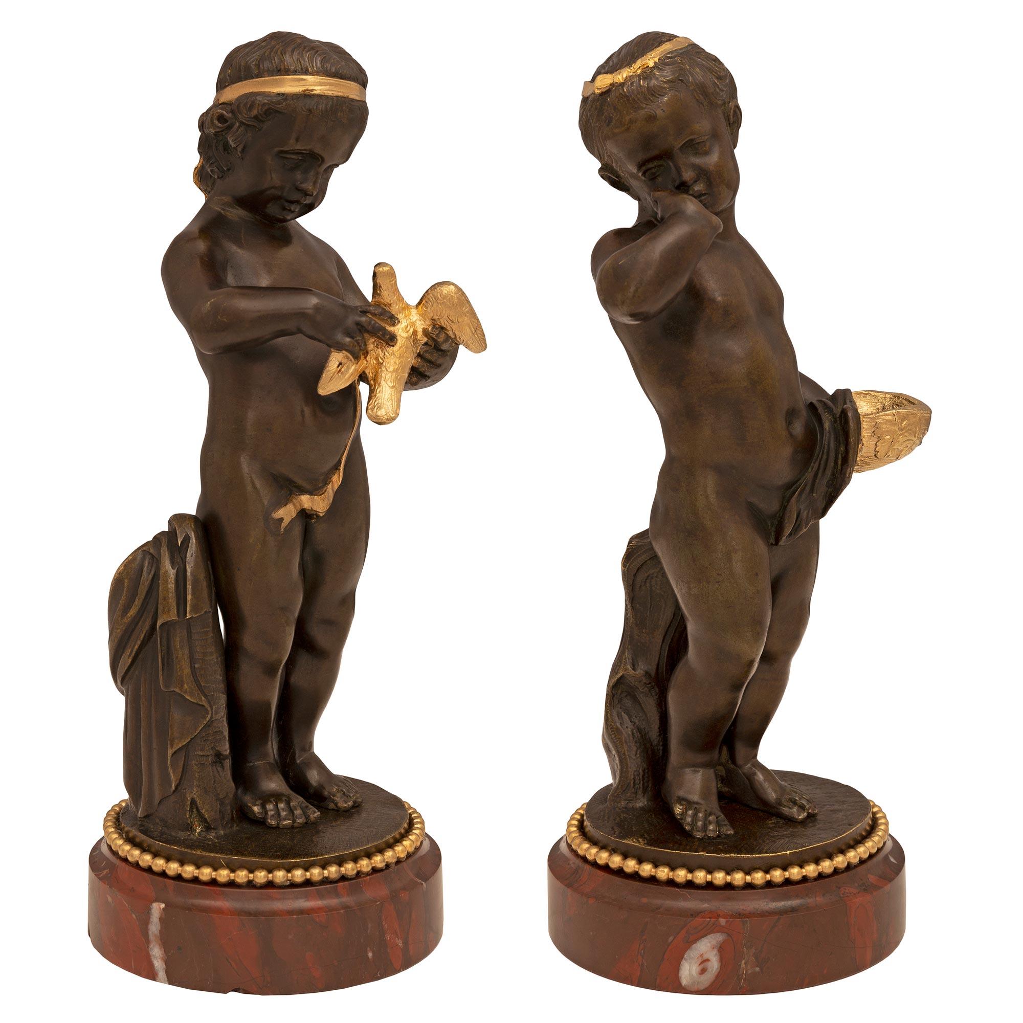 A most charming pair of French 19th century Louis XVI st. patinated bronzes, ormolu and Rouge Griotte marble statues. Each small scale statue is raised by an elegant circular Rouge Griotte marble base with a fine wrap around ormolu beaded band.