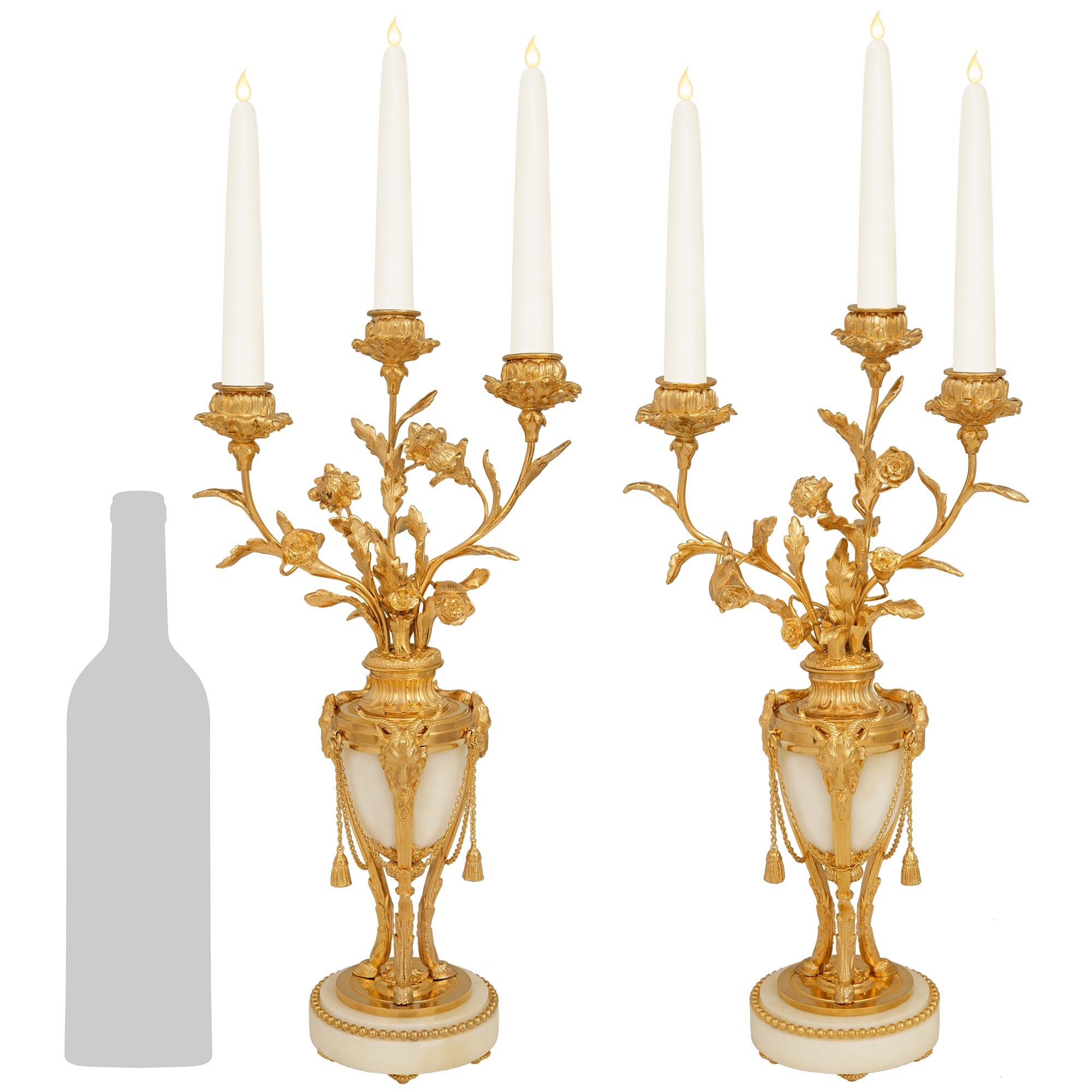 Elegante pareja de candelabros franceses del siglo XIX, estilo Luis XVI, de mármol blanco de Carrara y Ormolu. Esta impresionante pareja de candelabros de tres brazos se eleva sobre unas bases circulares de mármol blanco de Carrara decoradas con una