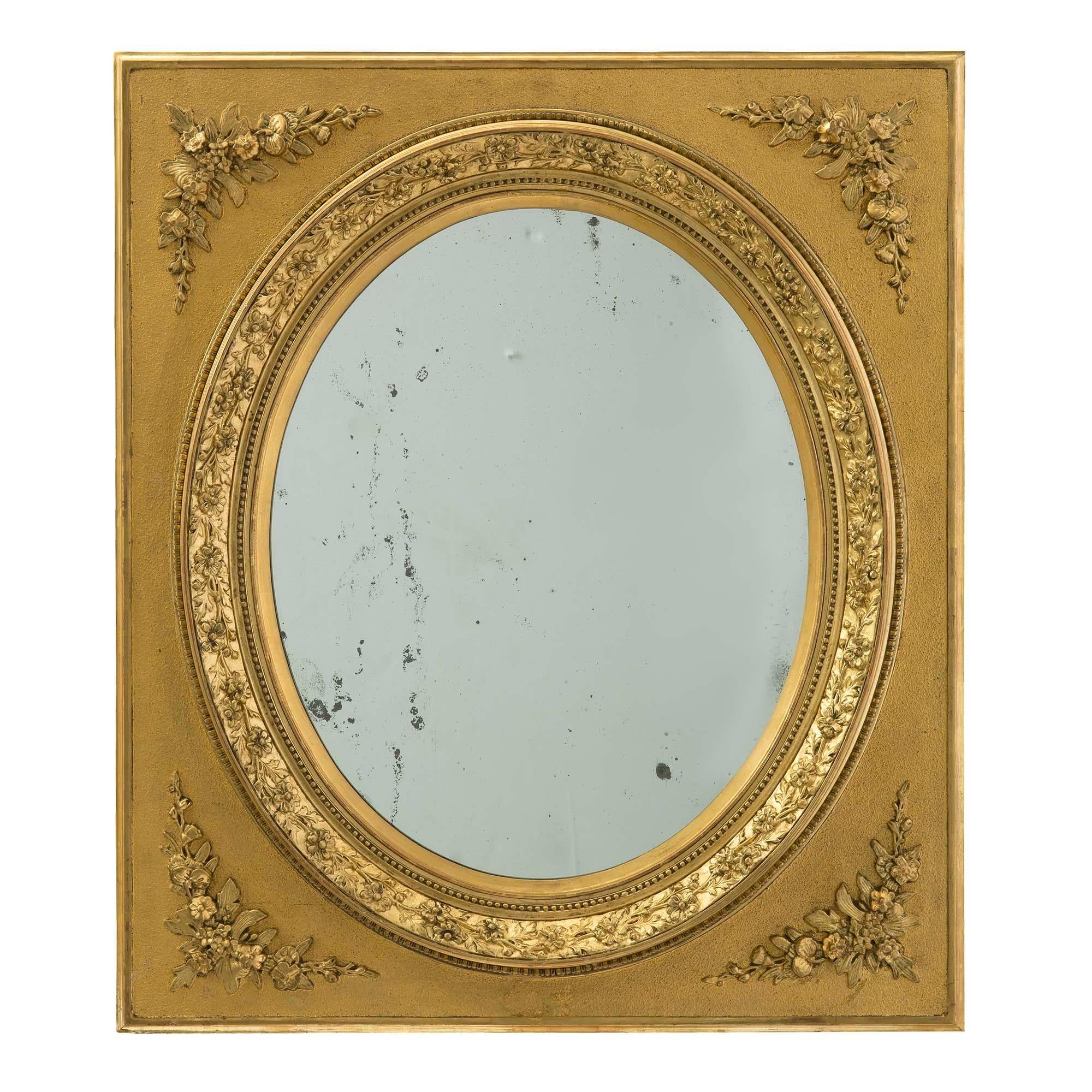 A pair of French 19th century Louis XVI St. gilt wood mirrors. Each mirror is within a square frame and oval cutout with foliate trim in a satin and burnished finish. At each corner are foliate garlands. These mirrors may be displayed vertically or