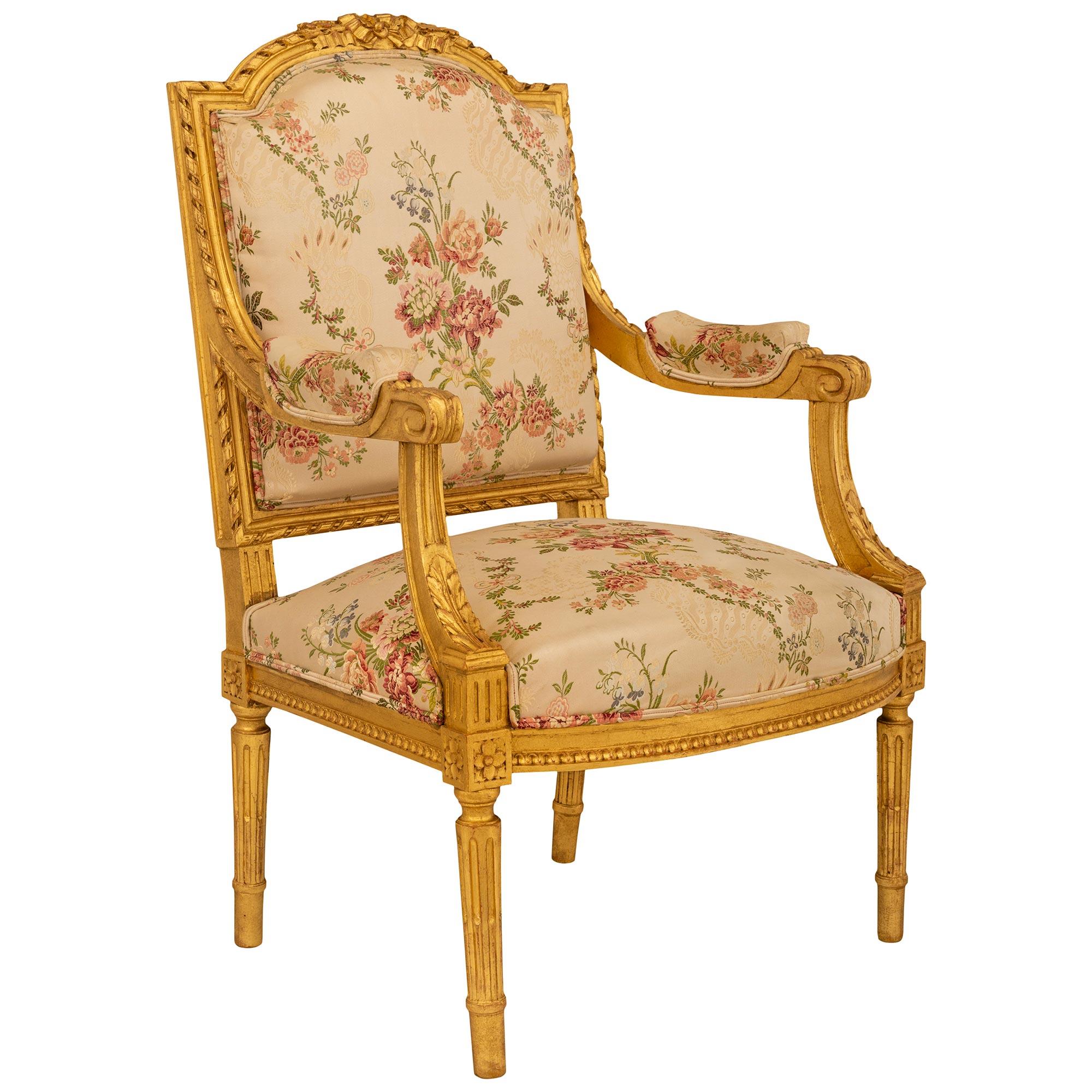 An elegant pair of French 19th century Louis XVI st. Giltwood armchairs. Each chair is supported by four round tapered and fluted Giltwood legs with richly carved rosette blocks atop each leg. The straight friezes on each side is decorated with