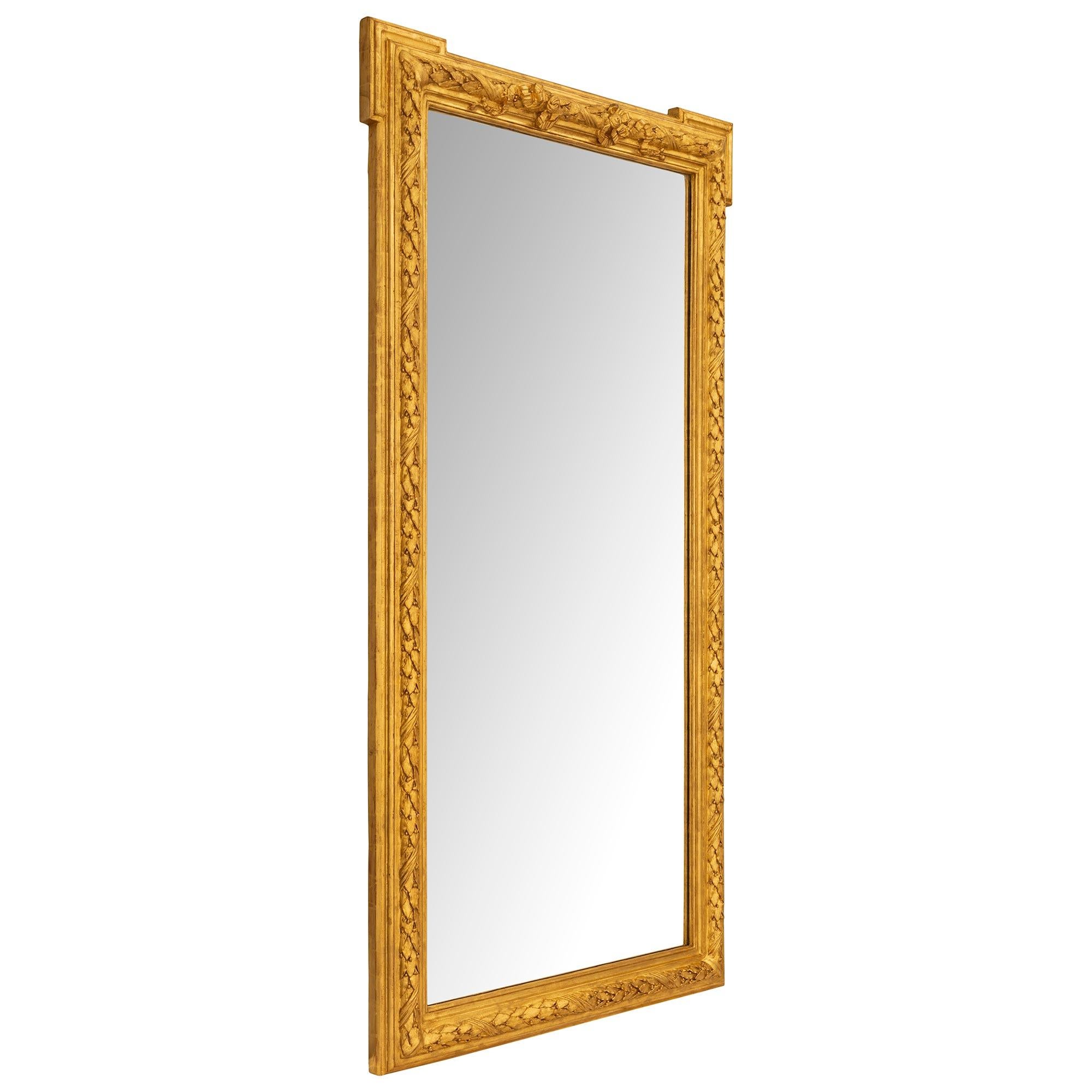 An elegant pair of French 19th century Louis XVI st. Giltwood mirrors. Surrounding each tall rectangular mirror plate is a detailed Giltwood frame with an inner and outer uninterrupted mottled edge. The center of the frame has a handsome and bold