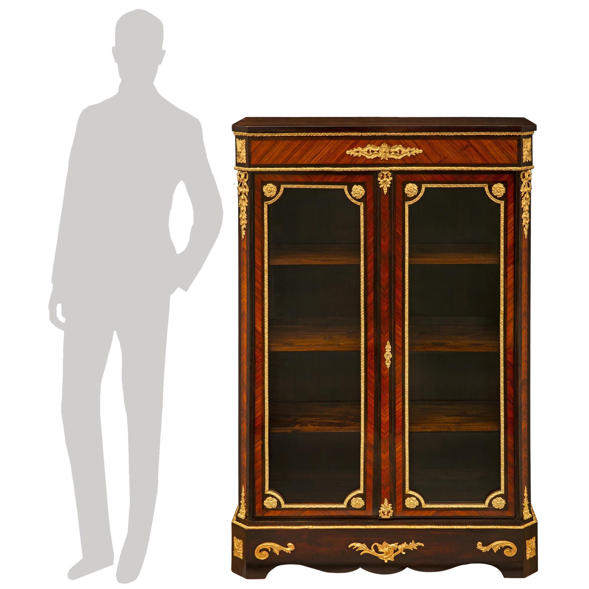 A striking and most elegantly pair of French 19th century Louis XVI st. Kingwood, Tulipwood and ormolu cabinet vitrines. Each two door vitrine is raised by fine block feet with delicate rosettes at each cut corner flanking the scalloped frieze