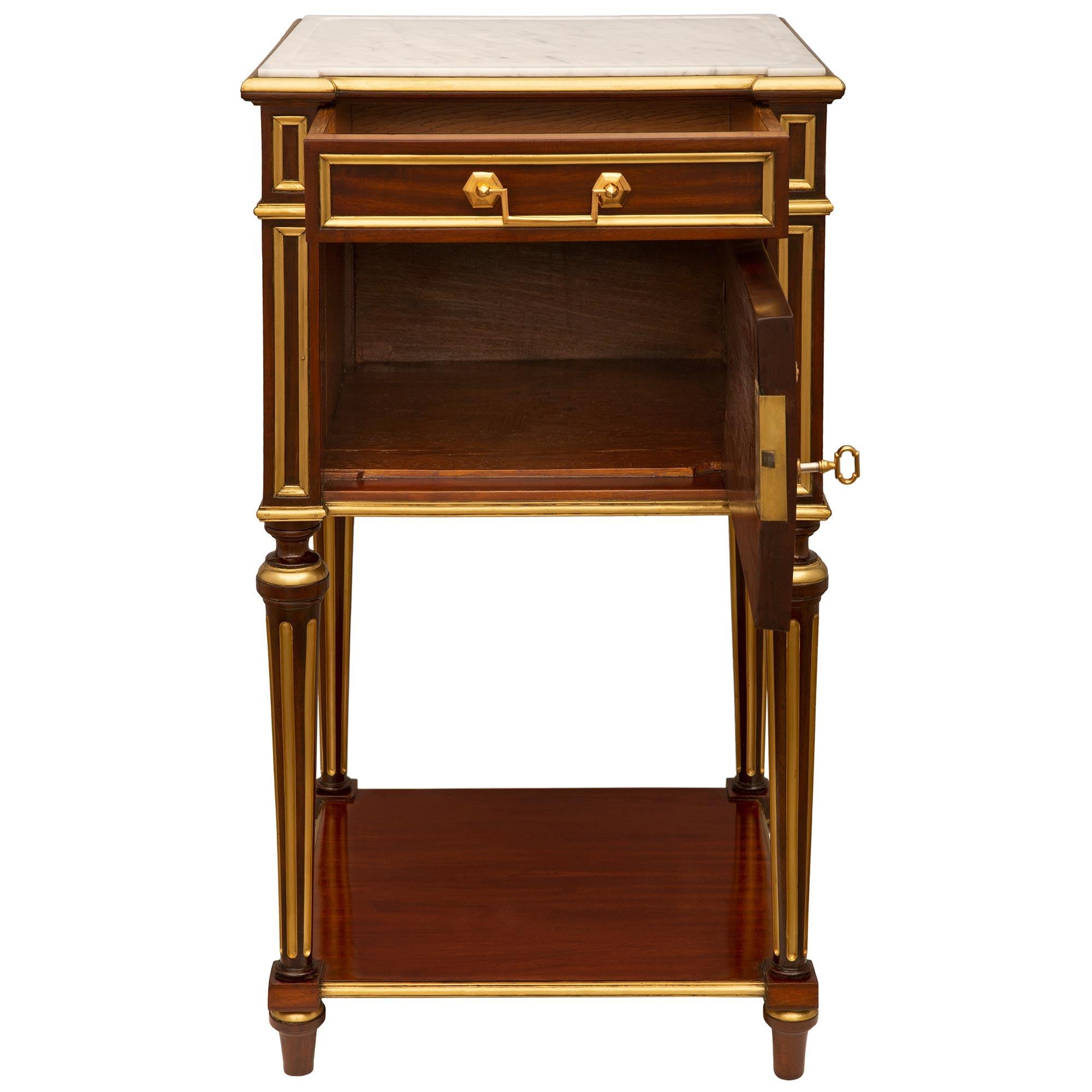 An elegant pair of French 19th century Louis XVI st. Mahogany, Brass, Ormolu and white Carrara marble side tables. The tables are raised on elegant topie shaped feet with brass rings connected by a square Mahogany stretcher, all below the circular