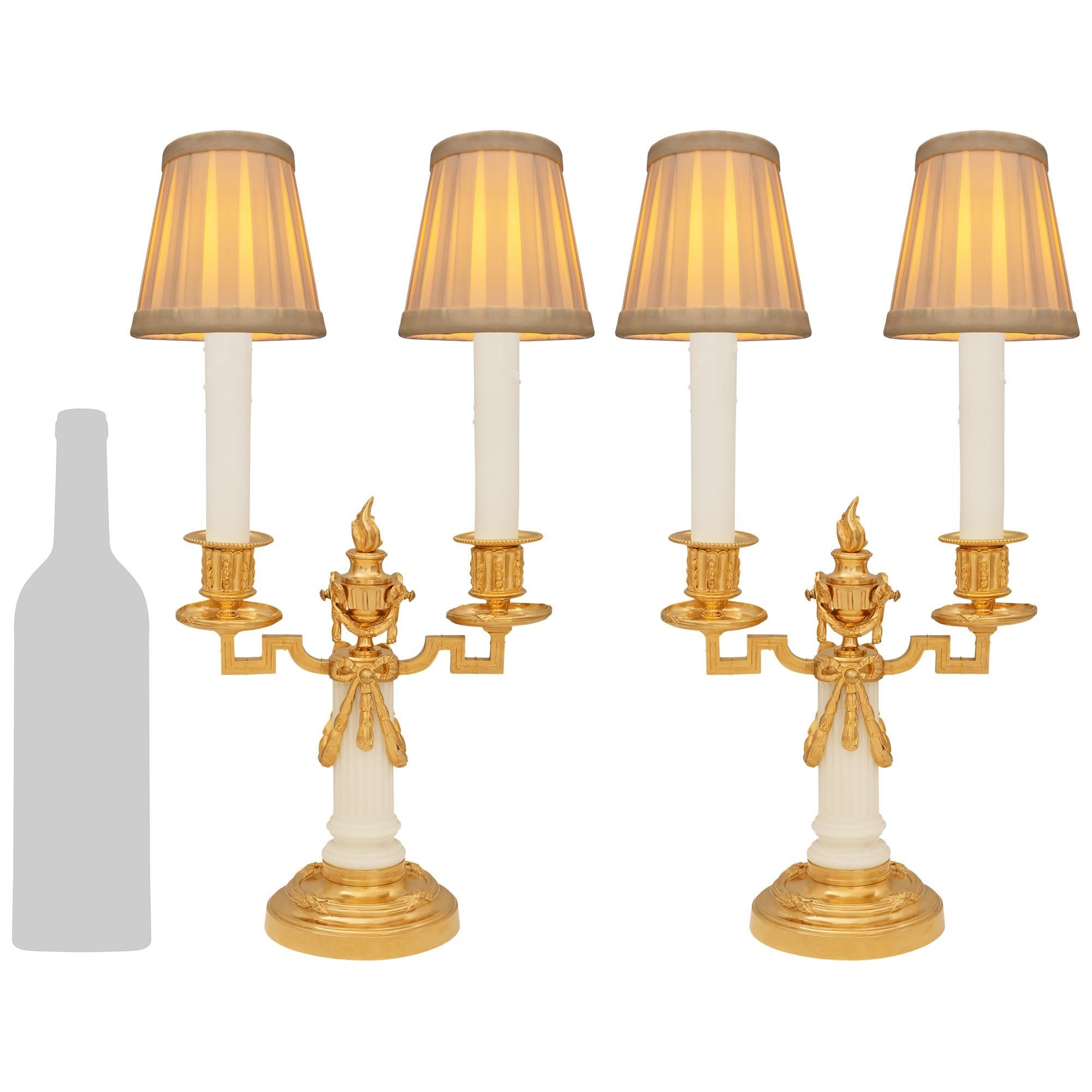 Un'affascinante coppia di lampade a candelabro francesi del XIX secolo in marmo bianco di Carrara e Ormolu. Ogni elegante candelabro elettrificato è sollevato da una base circolare in Ormolu decorata con bande screziate accentate da nastri