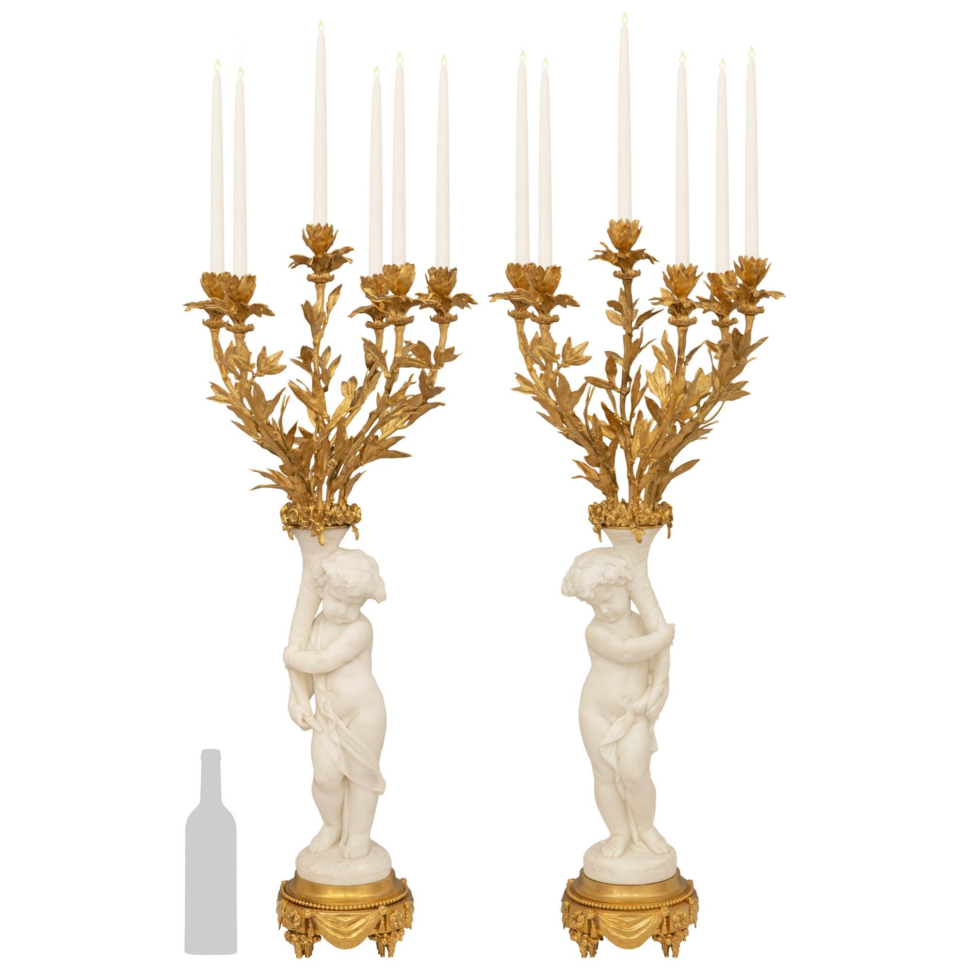 An exquisite and finely detailed pair of French 19th century Louis XVI st. white Carrara marble and Ormolu candelabras. Each beautiful six arm candelabra is raised on a circular Ormolu stepped pedestal decorated by swaging garments, foliate designs,