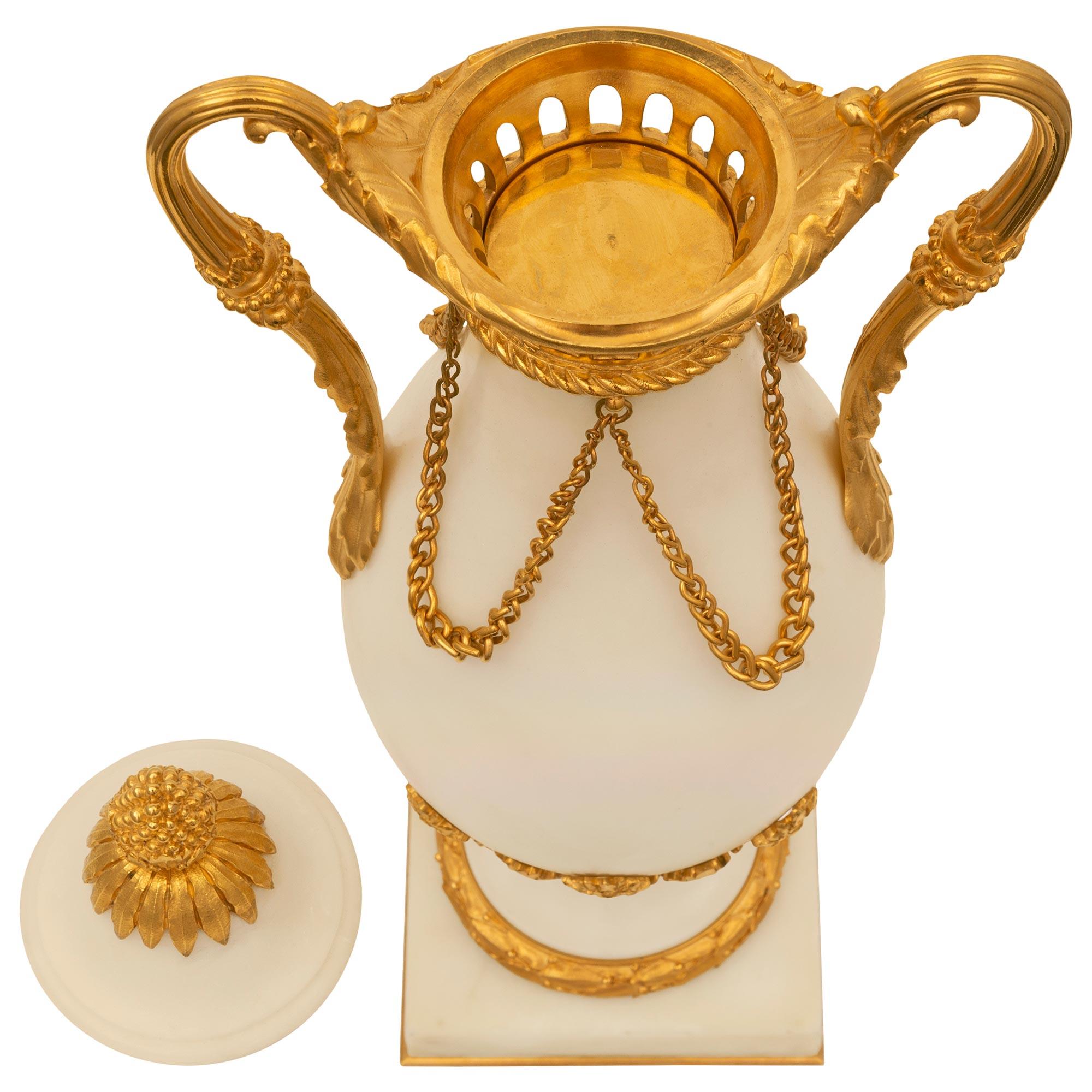 Paire d'élégantes urnes à couvercle en marbre blanc de Carrare et bronze doré, de style Louis XVI, datant du XIXe siècle. Chaque urne est surélevée par une base carrée avec un fin filet de fond en bronze doré sous le socle en forme de support décoré