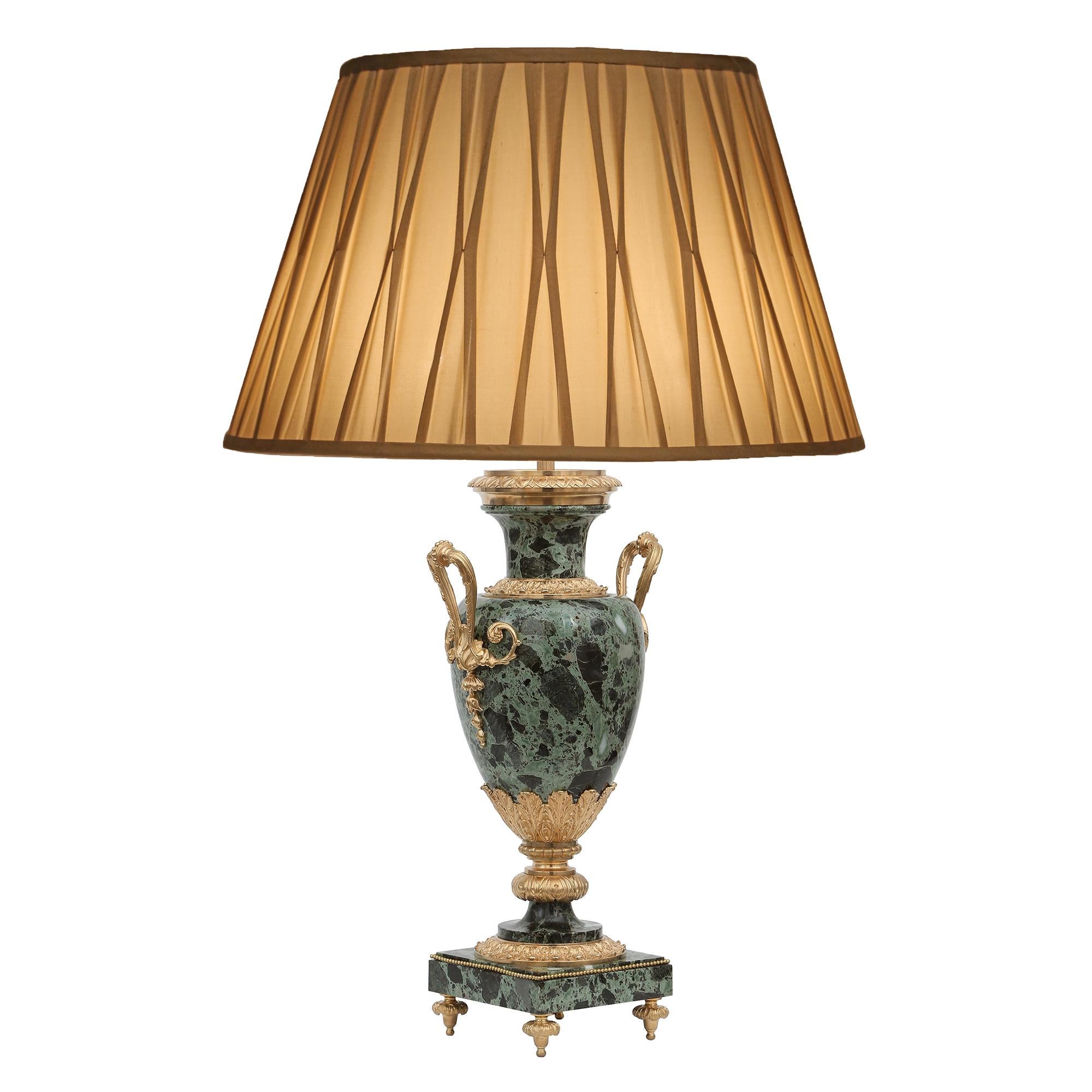 An elegant and high quality pair of French 19th century Louis XVI st. marble and ormolu mounted lamps. Each lamp is raised by fine floral topie shaped ormolu feet. The square Greek Antique Green marble base is decorated with a beaded ormolu band