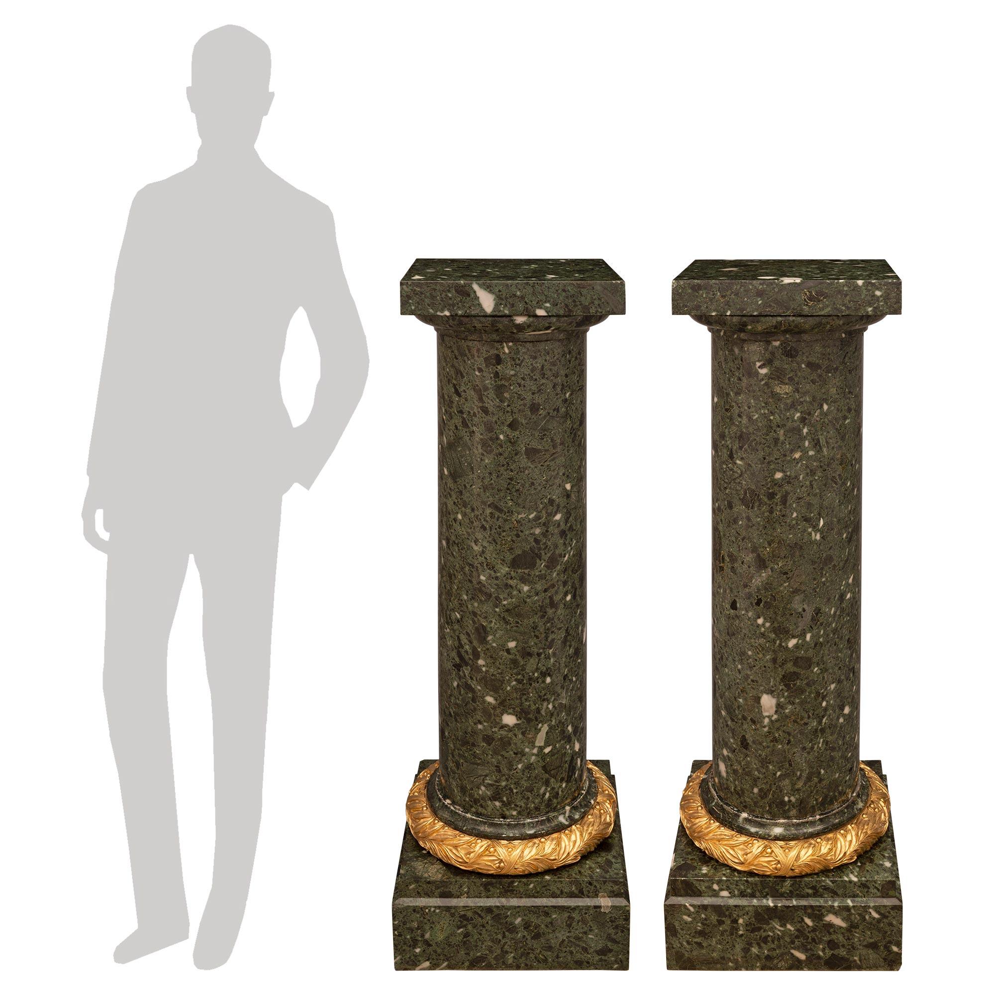 A stunning and monumentally scaled pair of French 19th century Louis XVI st. Brèche Verte marble and ormolu pedestal columns. Each pedestal is raised by an elegant square base with a fine mottled border and striking richly chased wrap-around ormolu