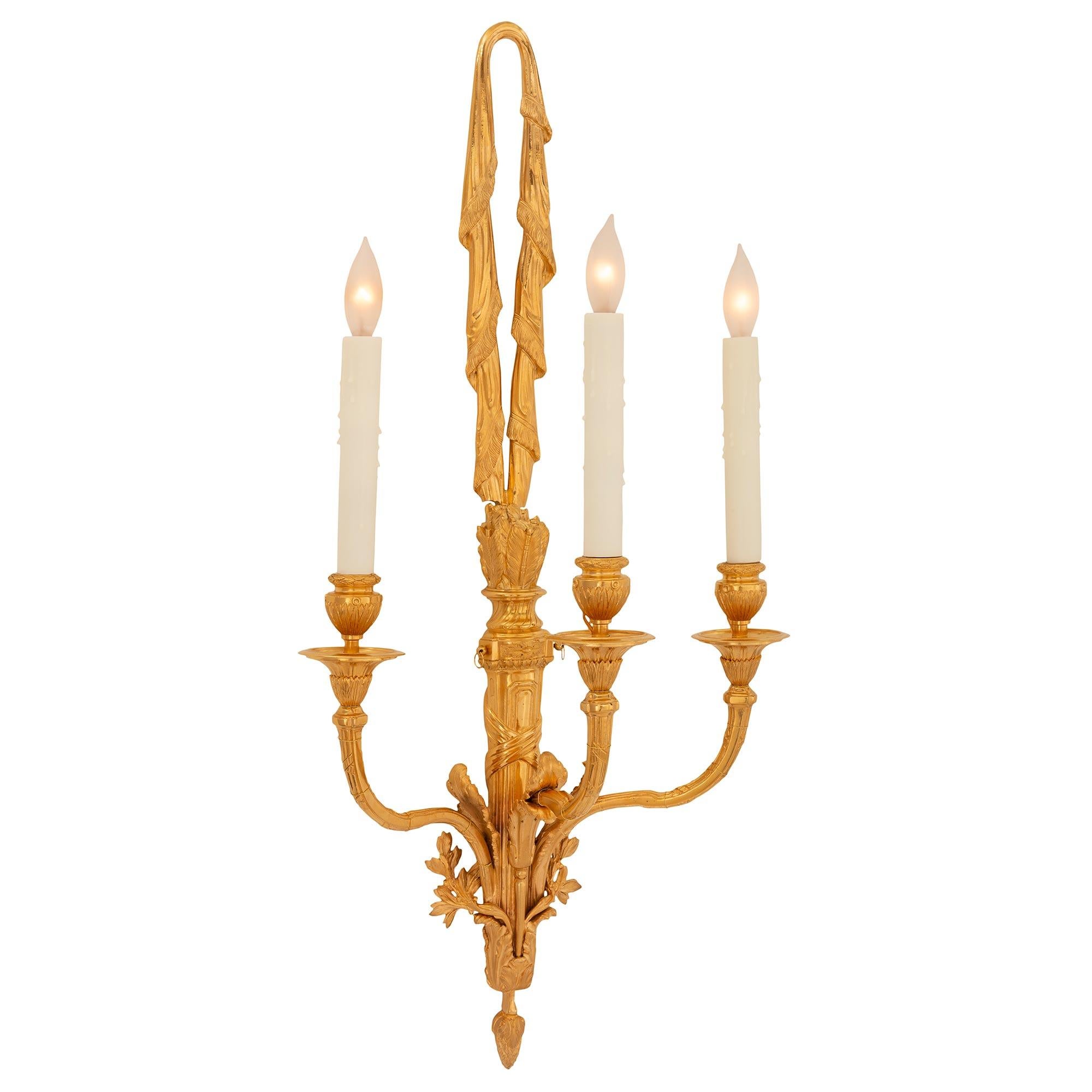 Une paire élégante et très décorative d'appliques en bronze doré d'époque Louis XVI et Napoléon III du XIXe siècle. Chaque applique unique à trois bras est centrée par un charmant épi de faîtage en forme de gland finement détaillé, entouré de