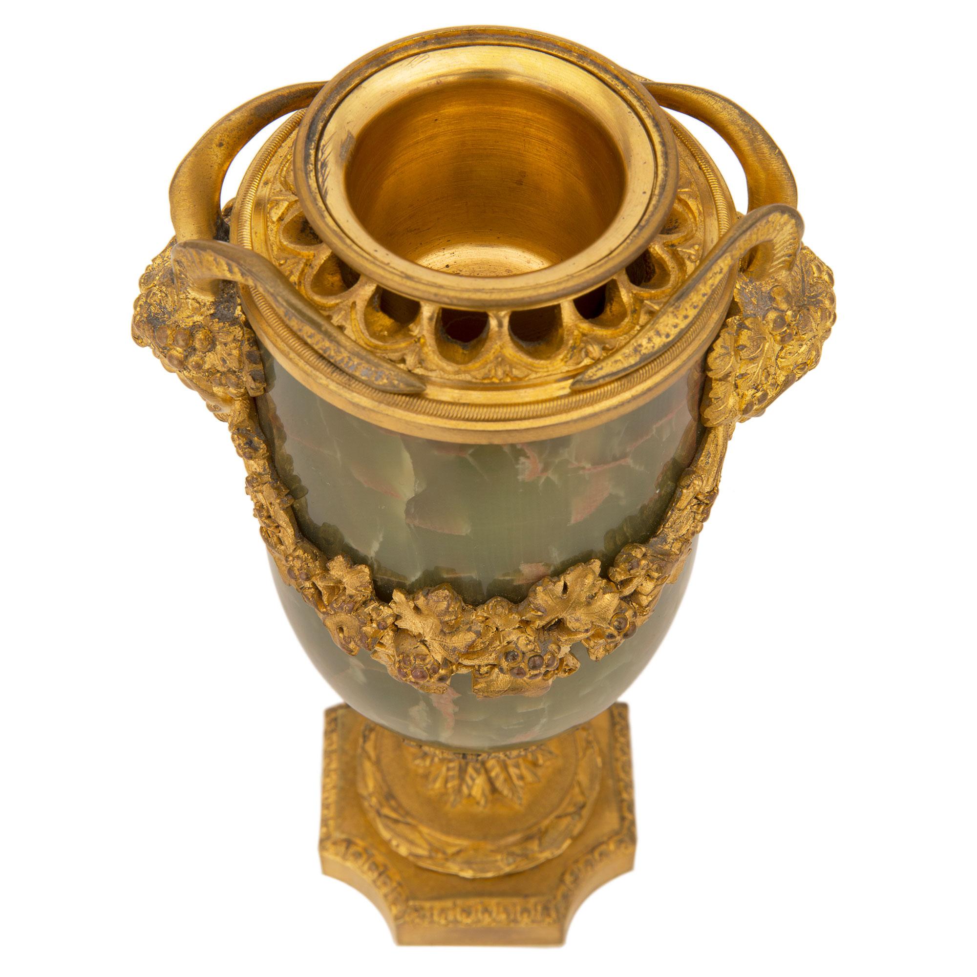 A remarkable pair of French 19th century Louis XVI st. onyx and ormolu lidded urns. Each urn is raised by a square ormolu base with concave corners and a delicate Coeur de Rai wrap around band. The socle shaped pedestals display Fine wrap around