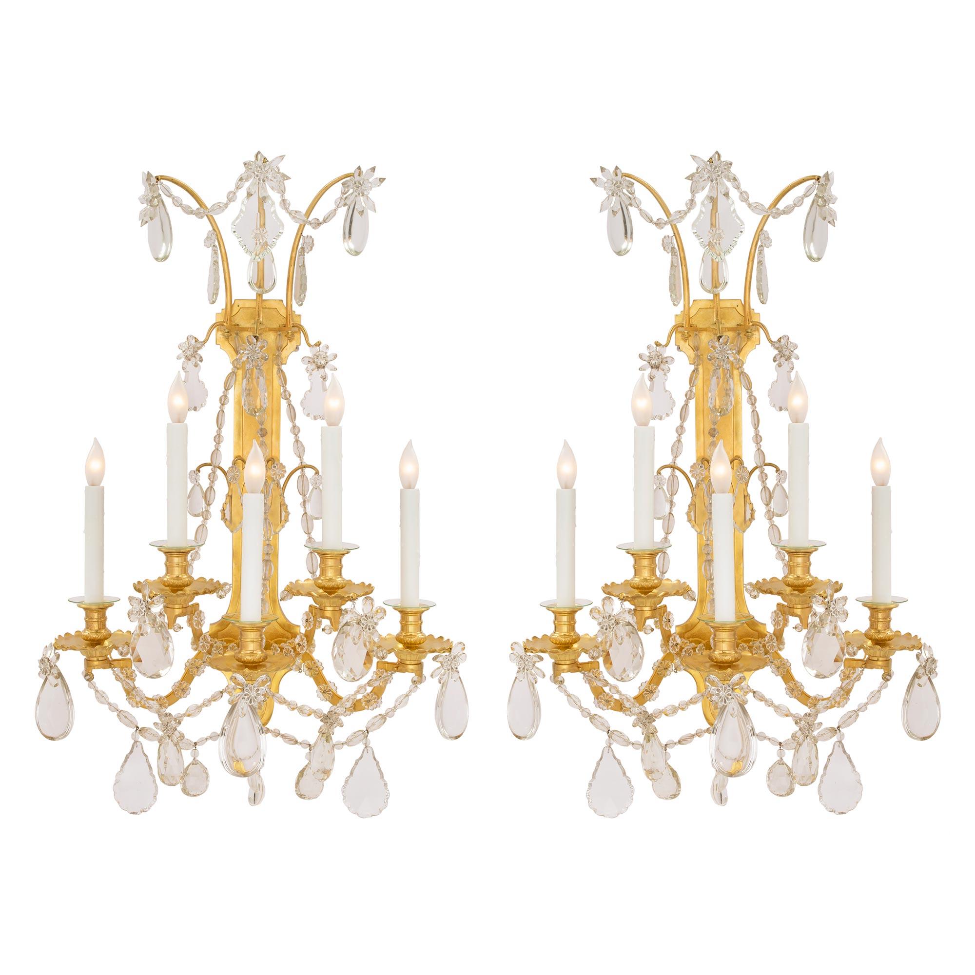 A beautiful pair of French 19th century Louis XVI st. ormolu and Baccarat crystal sconces. Each sconce displays a lovely back plate with a striking recessed textured design. The five scrolled arms are decorated with fine crystal rosettes and
