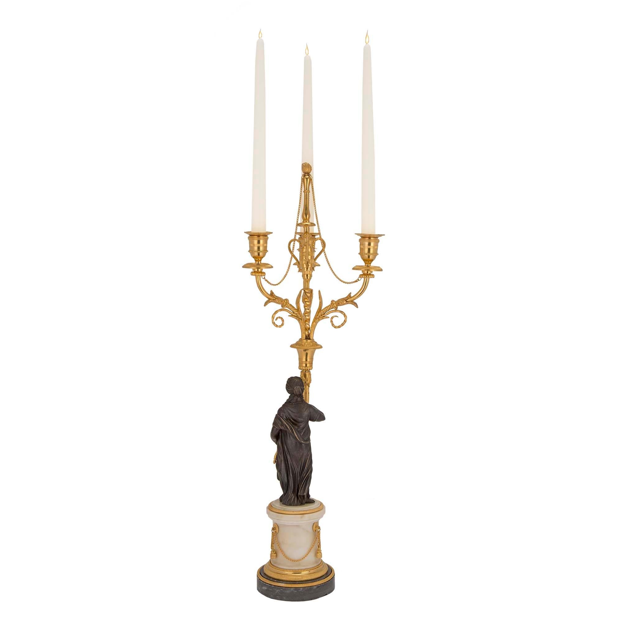 Una bellissima coppia di candelabri francesi del XIX secolo in stile Luigi XVI in ormolu e bronzo patinato. Ogni candelabro a tre bracci poggia su una base circolare in marmo Gris St. Anne con una fascia ormeggiata. Sopra c'è una colonna in marmo