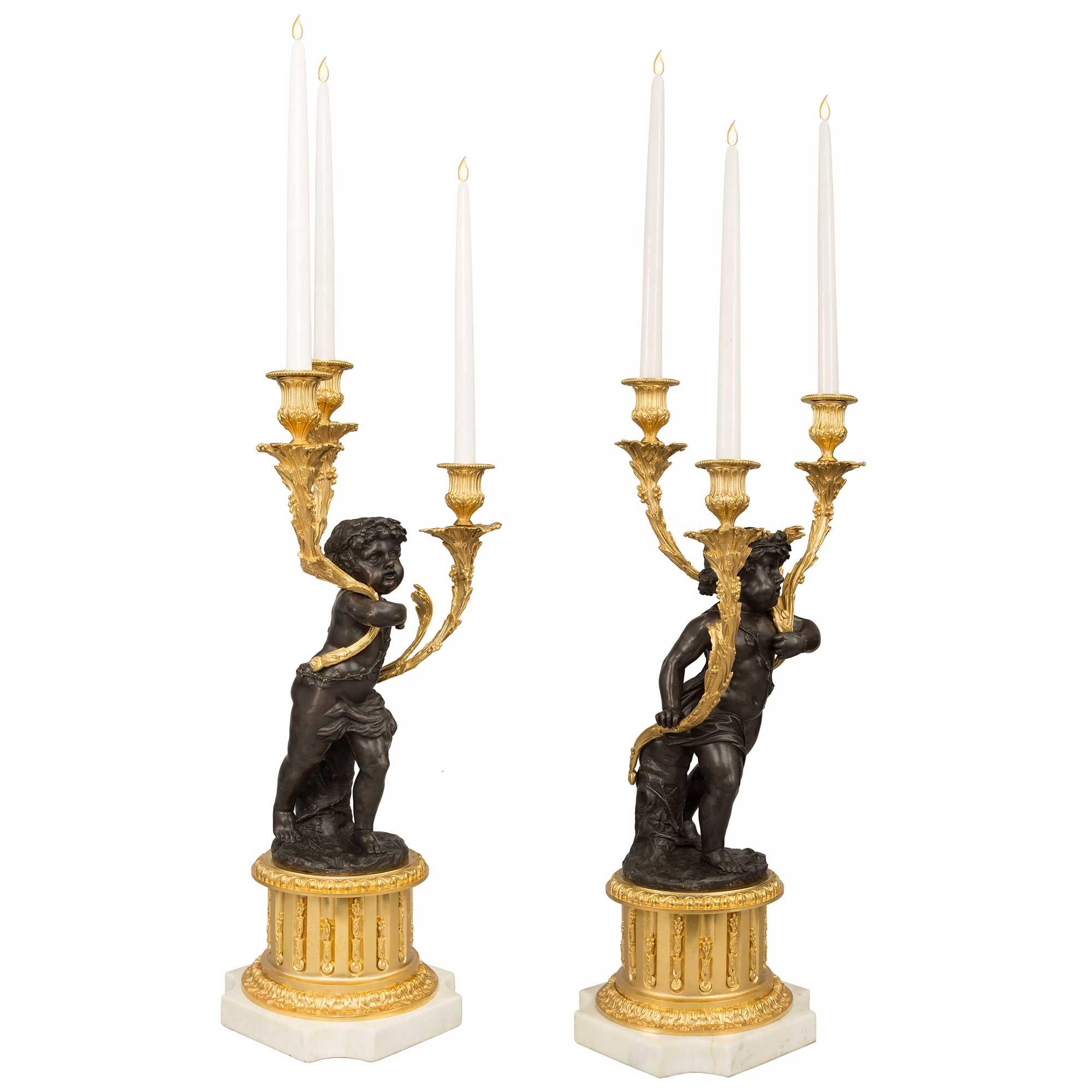 A very high quality true pair of French 19th century Louis XVI st. ormolu and patinated bronze, three arm candelabras. Each beautiful candelabra is raised by a square white Carrara marble base with concave corners. The ormolu socle pedestal displays