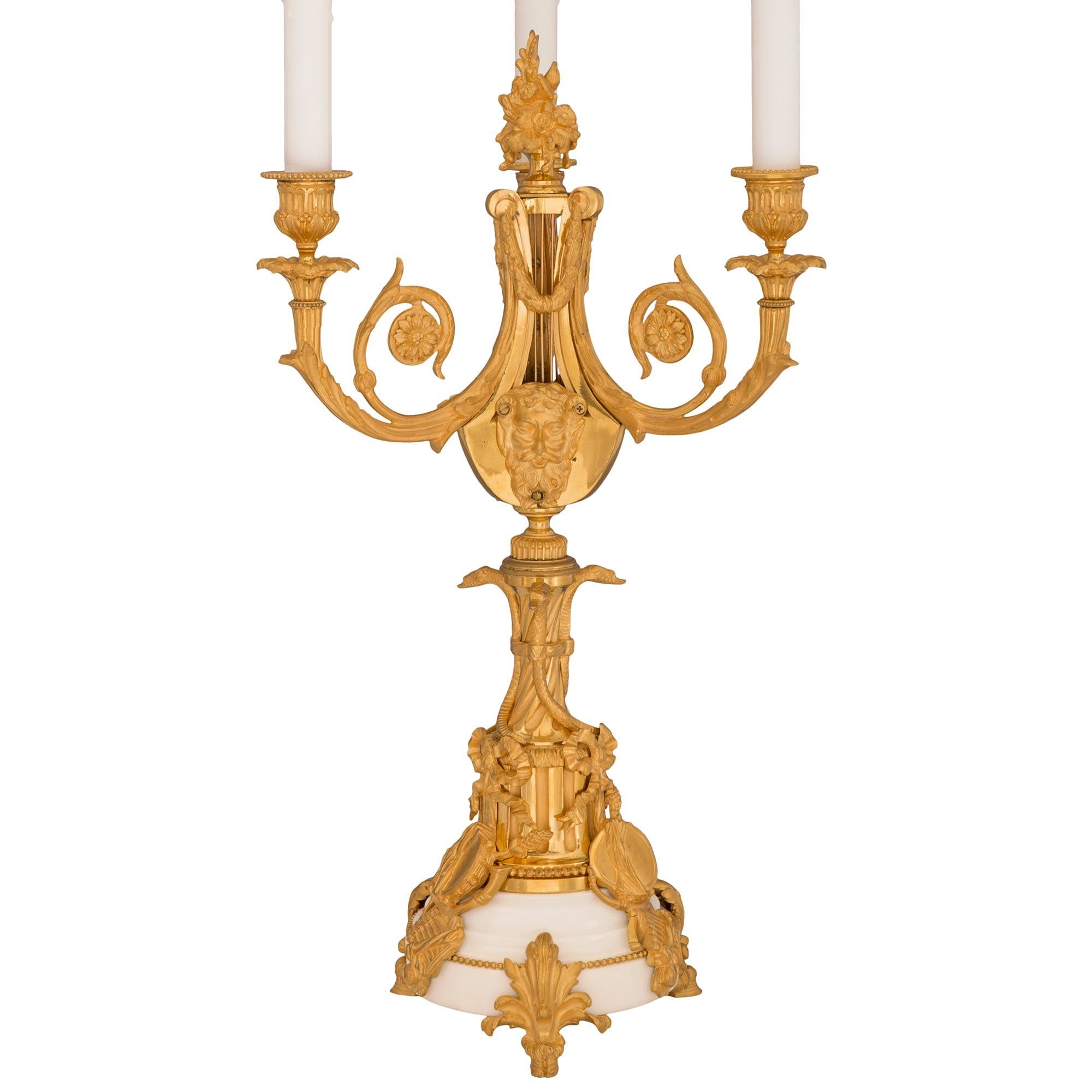 A striking pair of French 19th century Louis XVI st. ormolu and white Carrara marble candelabra lamps. Each three arm lamp is raised by an elegant circular stepped white Carrara marble base and striking hoof feet with richly chased scrolled acanthus