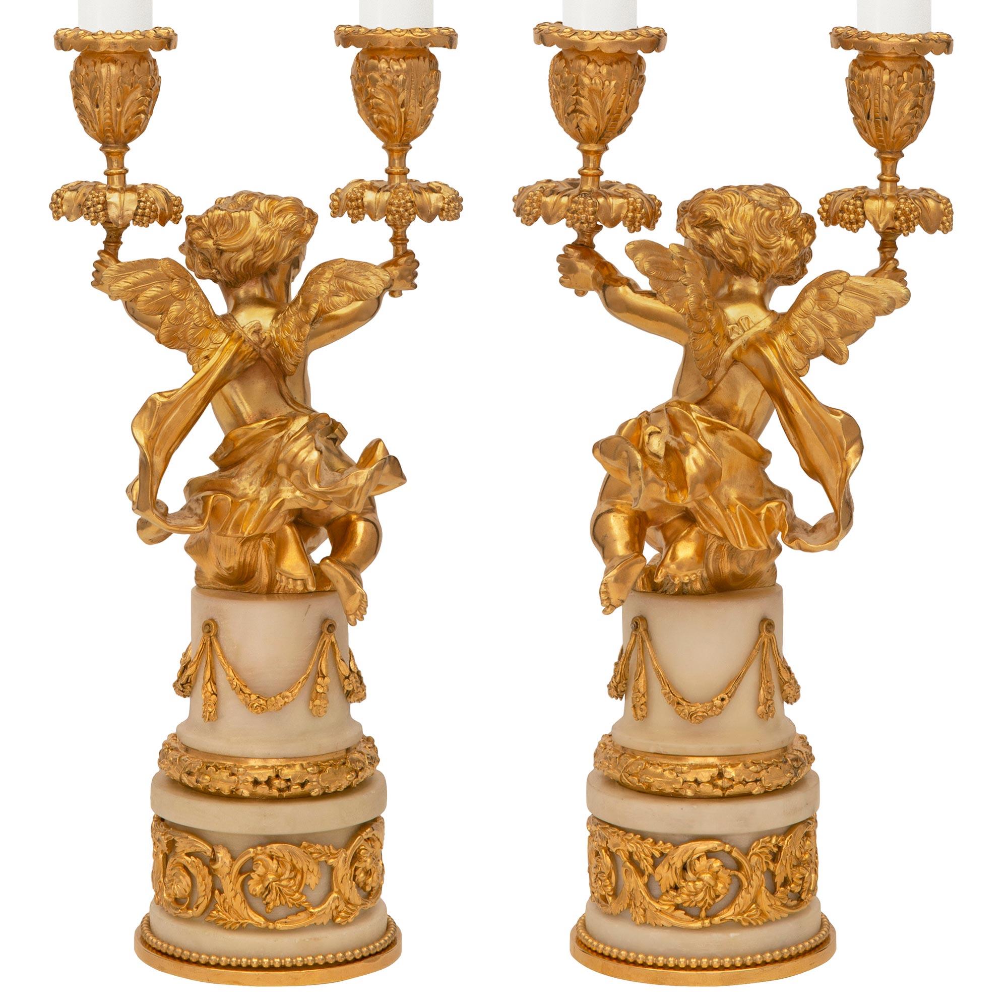 Une charmante paire de candélabres en marbre de Carrare blanc et bronze doré de style Louis XVI du 19ème siècle de très haute qualité. Chaque candélabre à deux bras est surélevé par une base circulaire en marbre blanc de Carrare avec une fine