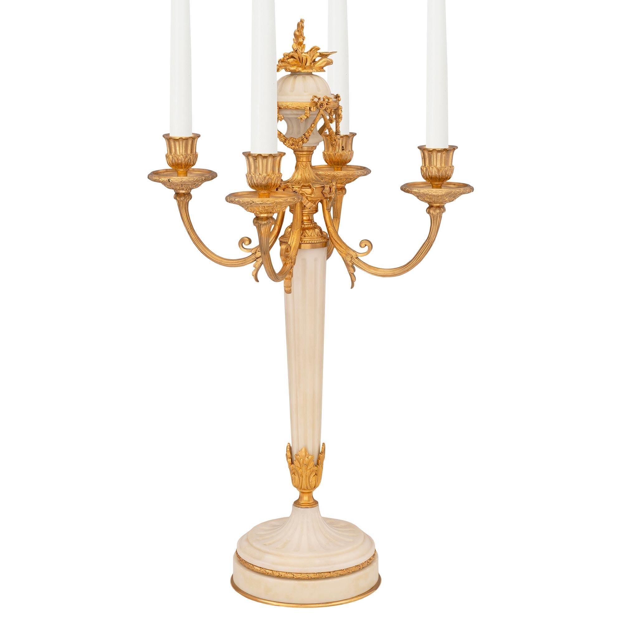 A beautiful and extremely elegant pair of French 19th century Louis XVI st. ormolu and white Carrara marble candelabras. Each unique four arm candelabra is raised by a circular white Carrara marble base with a fine bottom ormolu fillet and a richly