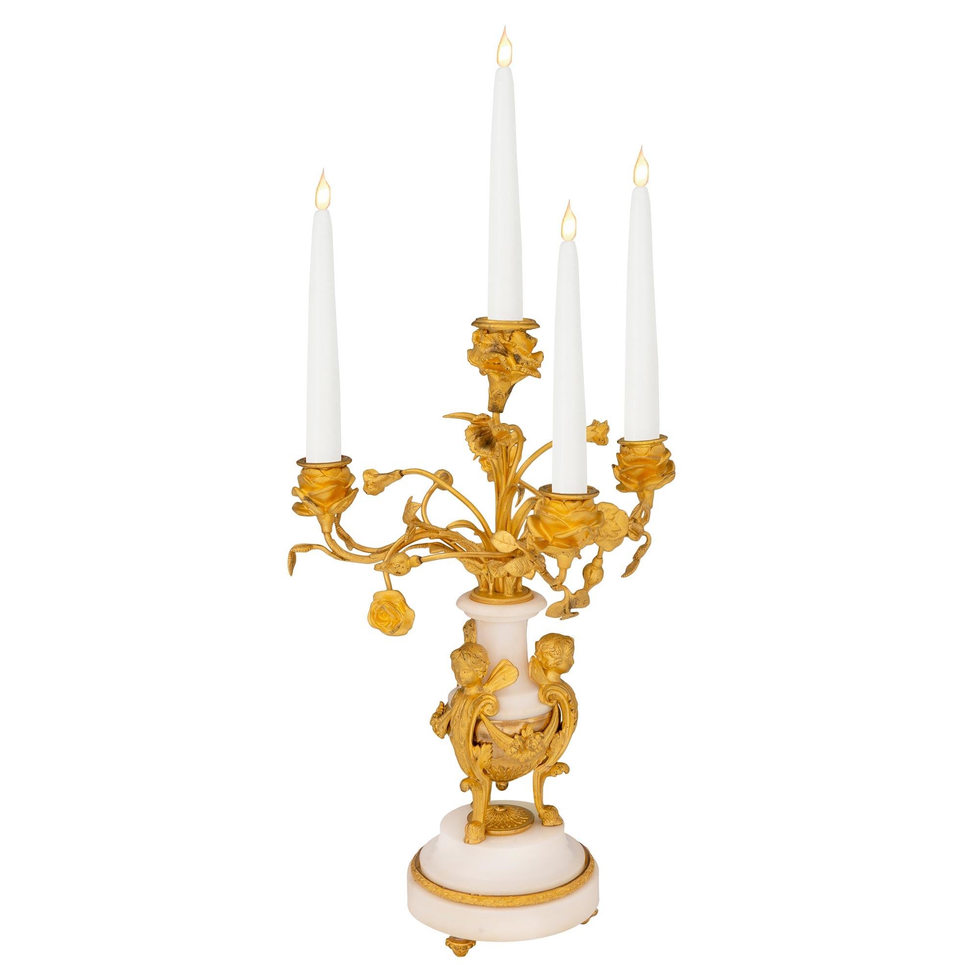 A beautiful and high quality pair of French 19th century Louis XVI st. ormolu and white Carrara marble four arm candelabras. Each candelabra is raised by fine ormolu topie shaped feet below a circular white Carrara marble base decorated with a