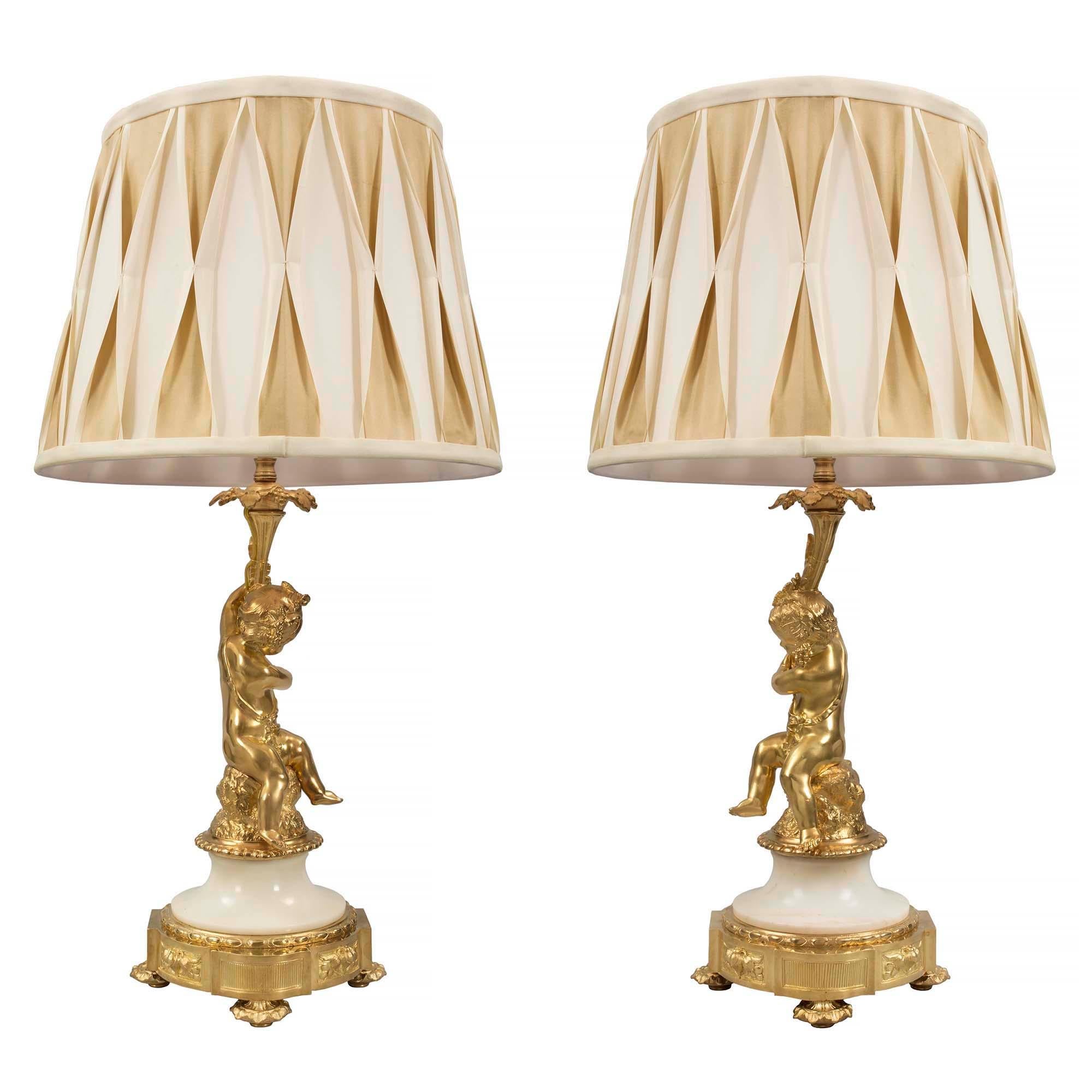 A wonderful pair of whimsical French 19th century Louis XVI st. ormolu and marble lamps. Each lamp is raised on a foliate topie feet below the circular base with protruding rectangular blocks and foliate panels. Above the white Carrara marble socle