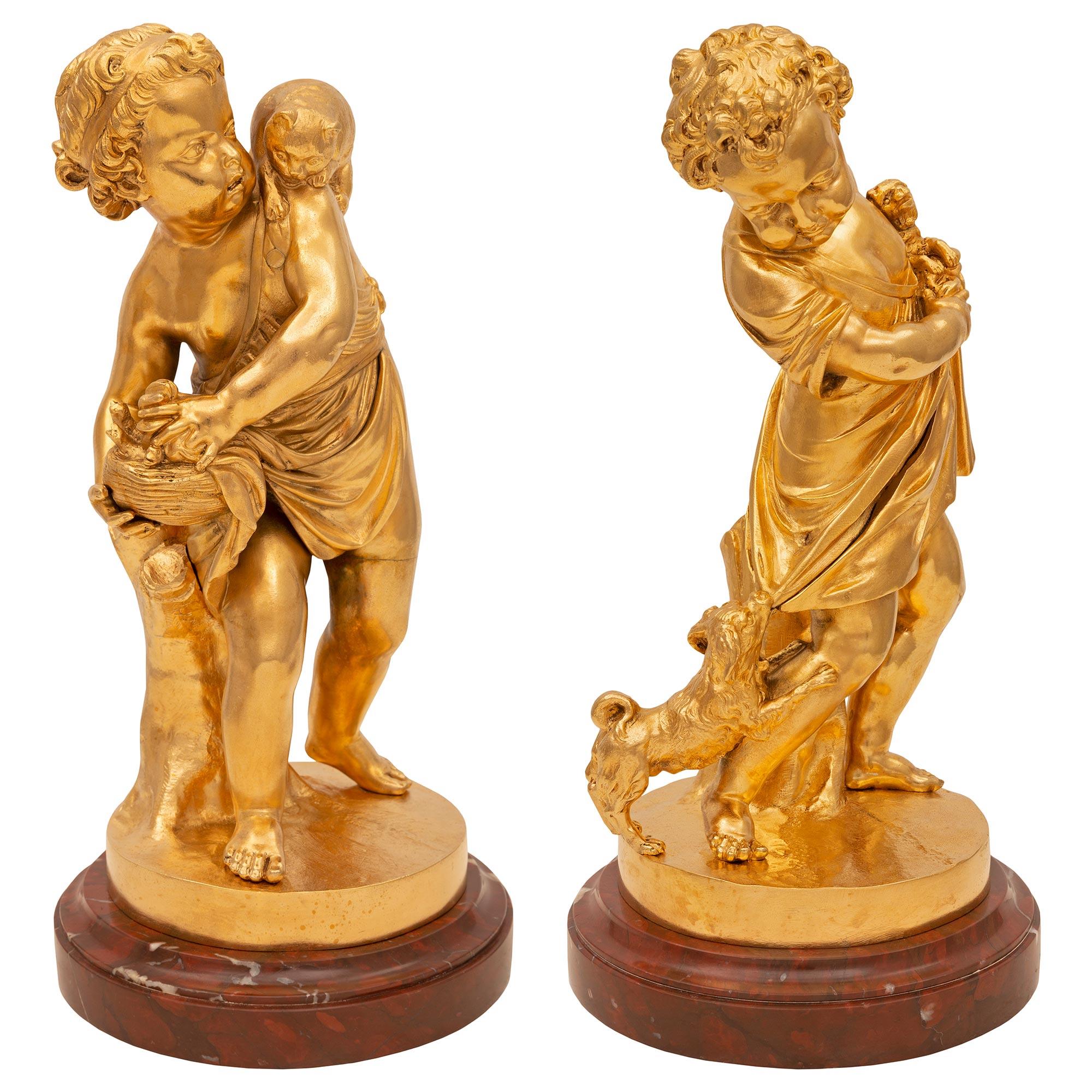 An exceptional and most charming true pair of French 19th century Louis XVI st. ormolu and Rouge Griotte marble statues. Each statue is raised by a Fine circular Rouge Griotte marble base with an elegant wrap around mottled border. The statues above